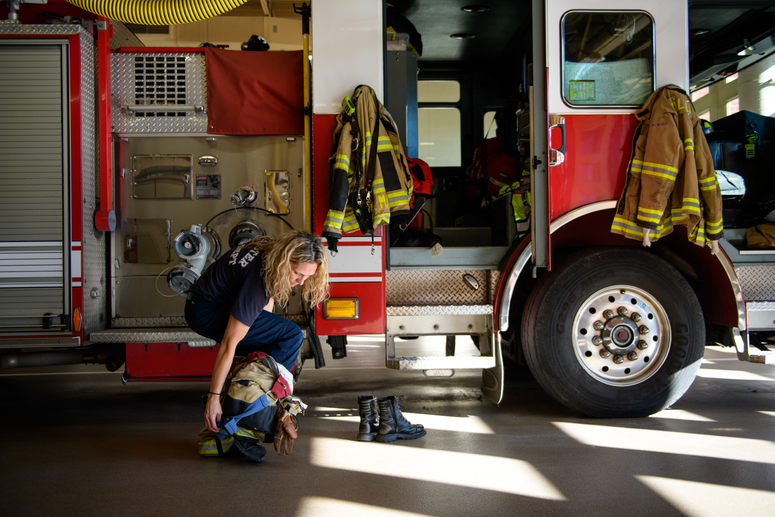 a female firefighter pulling up turnout gear in front of a fire engine