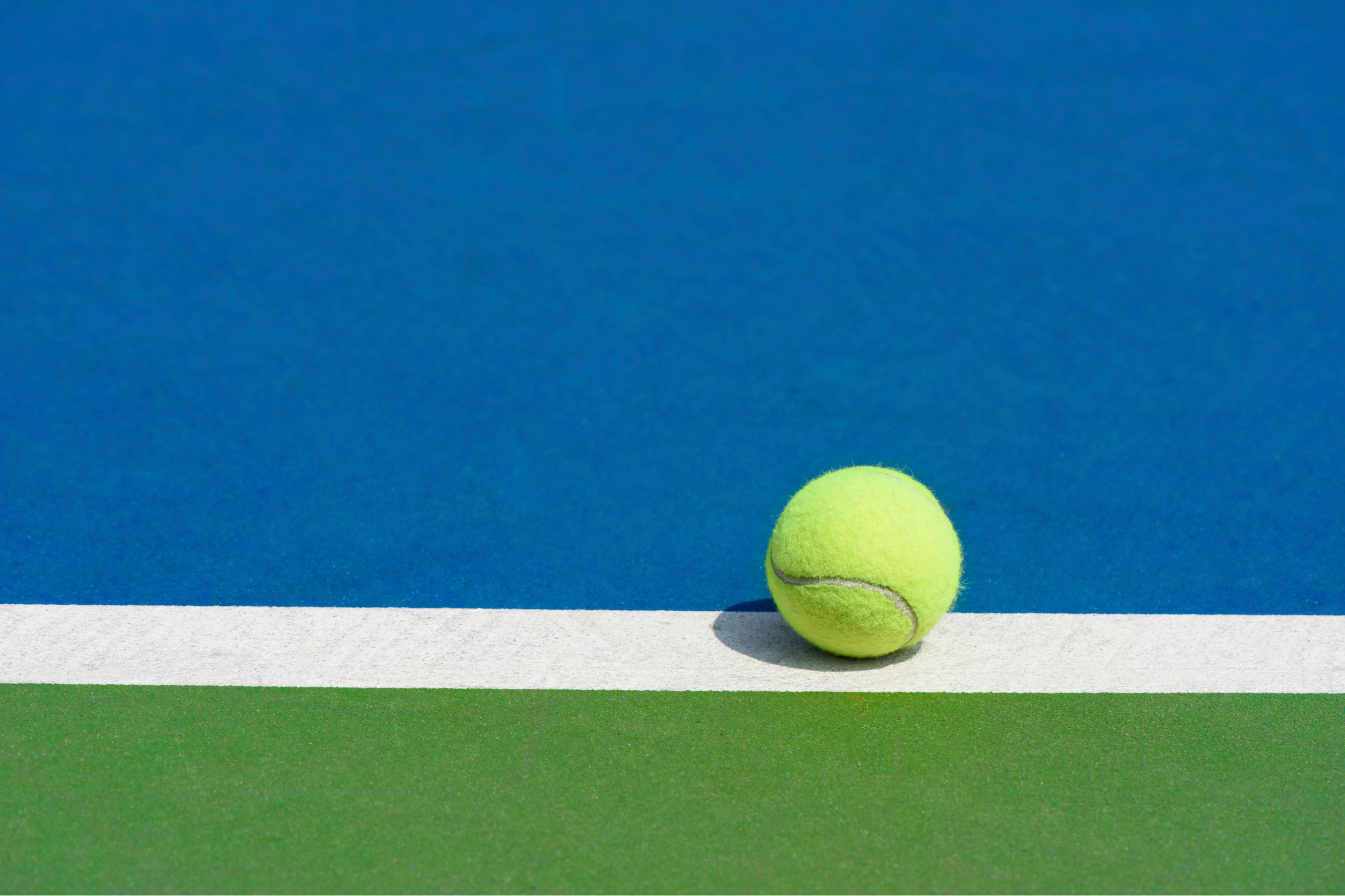 a bright green tennis ball rested on the white line of a blue and green tennis court