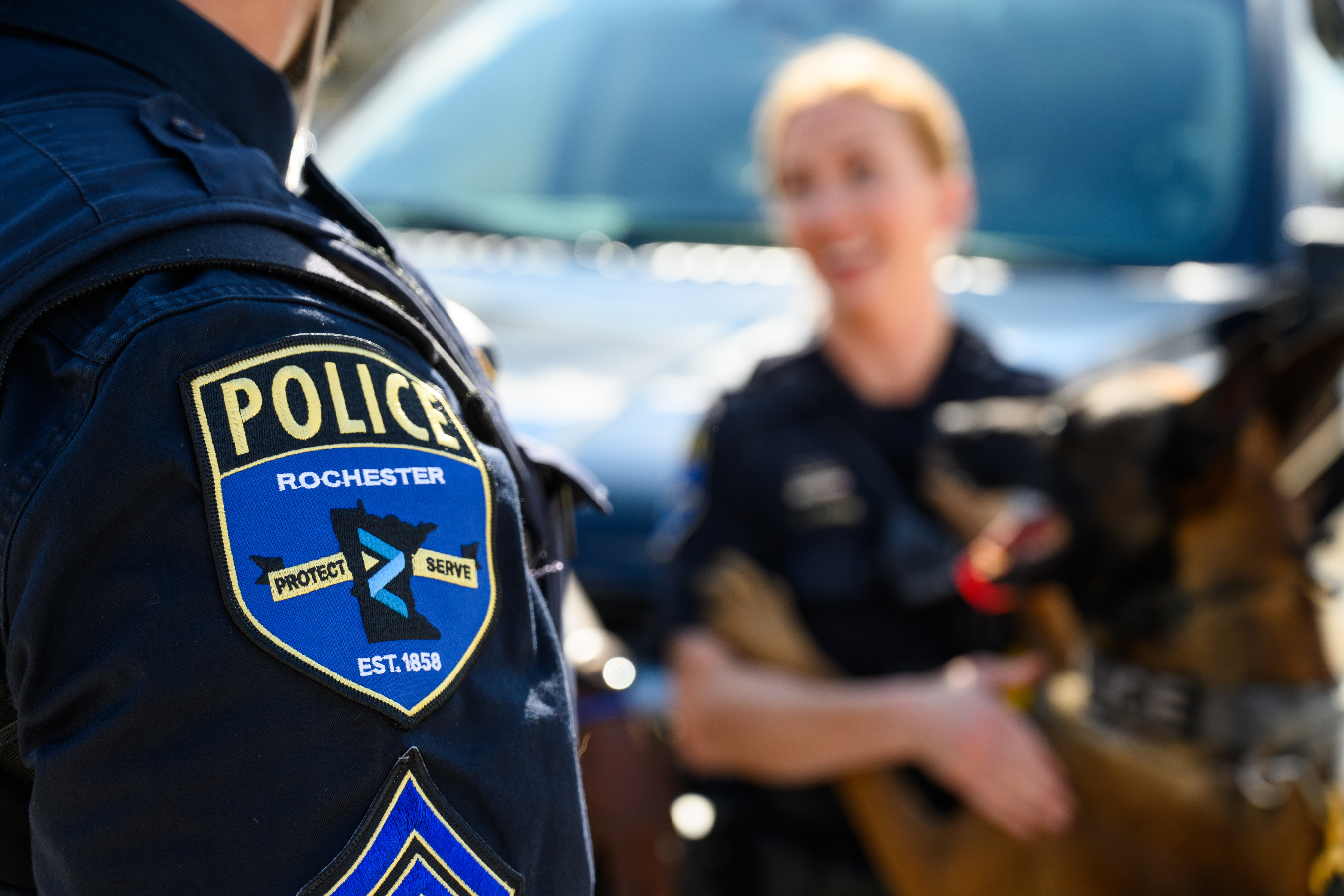 an rpd patch on the shoulder of a uniform with another officer and k9 in the background