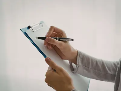 A person's hands holding a clipboard and pen about to write on a blank piece of paper
