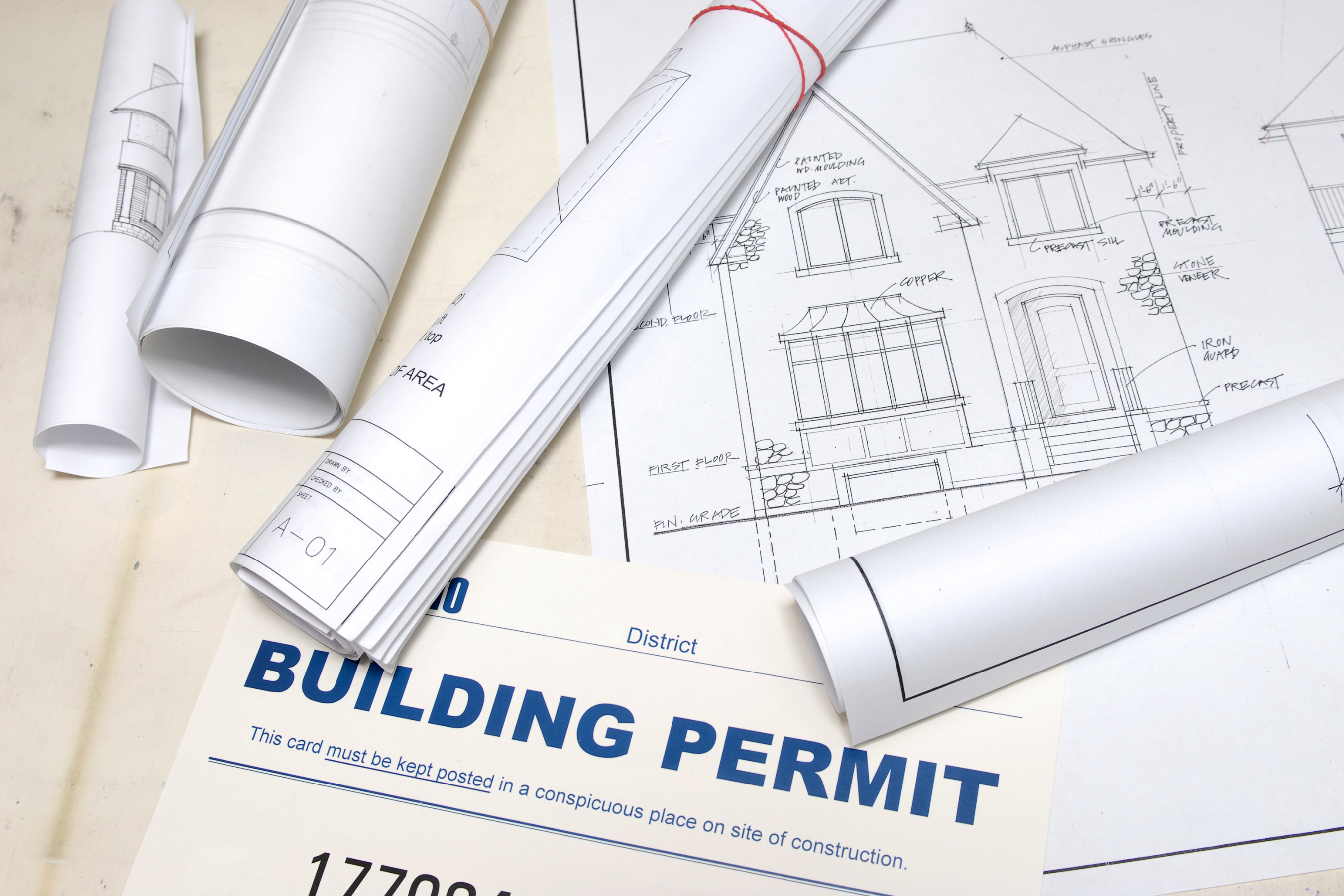 A building permit on a table littered with building plans and blueprints