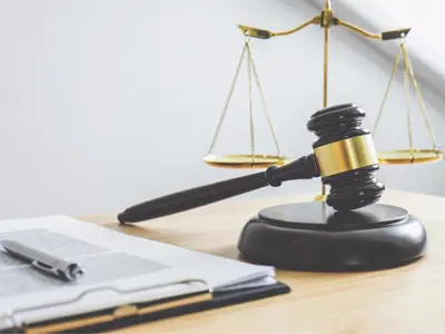 a gavel in front of a small set of justice weights on a desk with a clipboard of papers and a pen