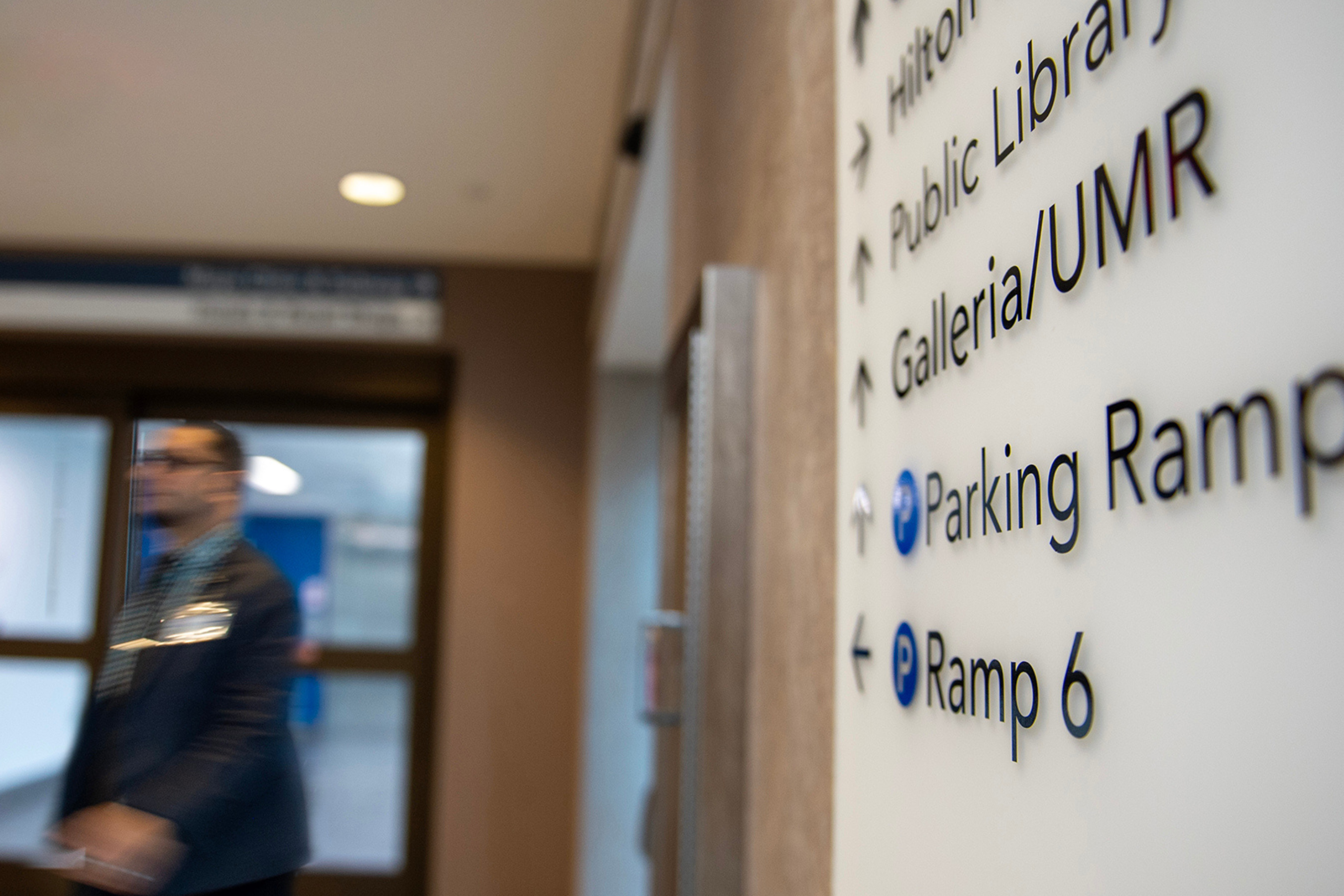 a wayfinding sign pointing toward parking options with people walking out of focus in the background
