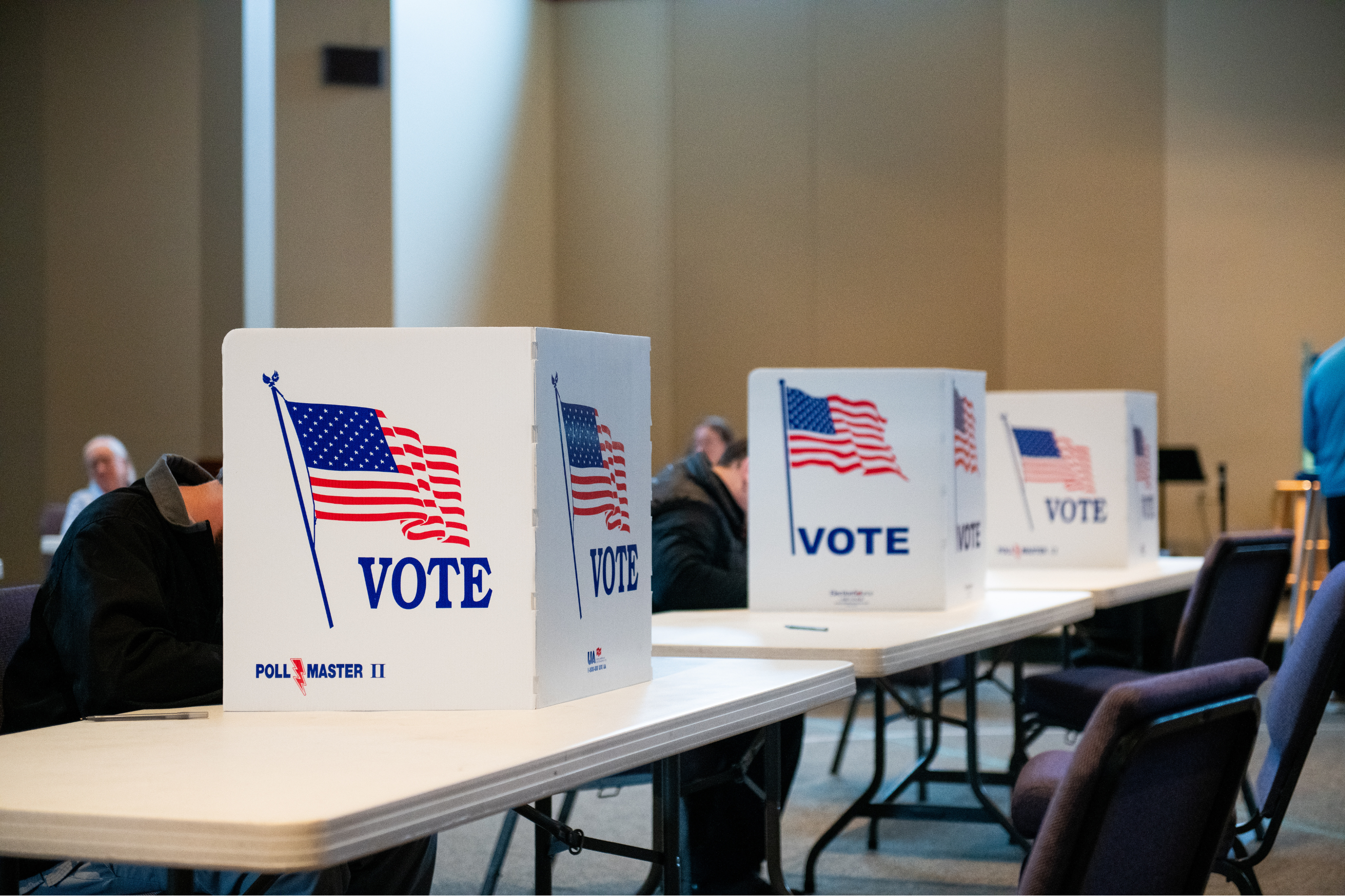 A row of ballot boxes with unidentifiable people behind them.
