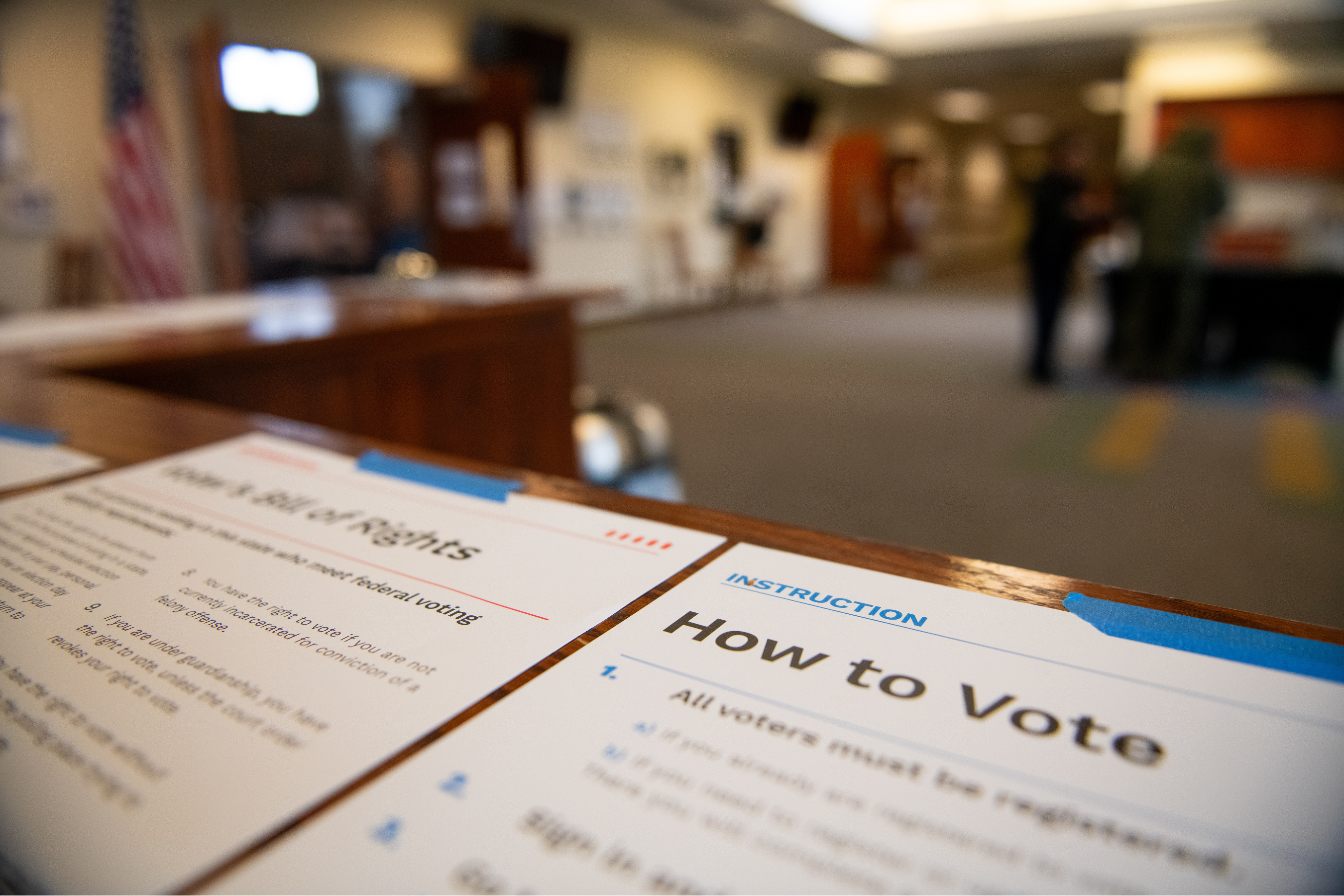 blurred image of paper voting instructions taped to a wooden surface with a polling place in the background