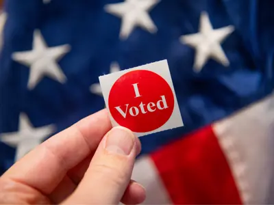 a red 'i voted' sticker being held in front of an american flag