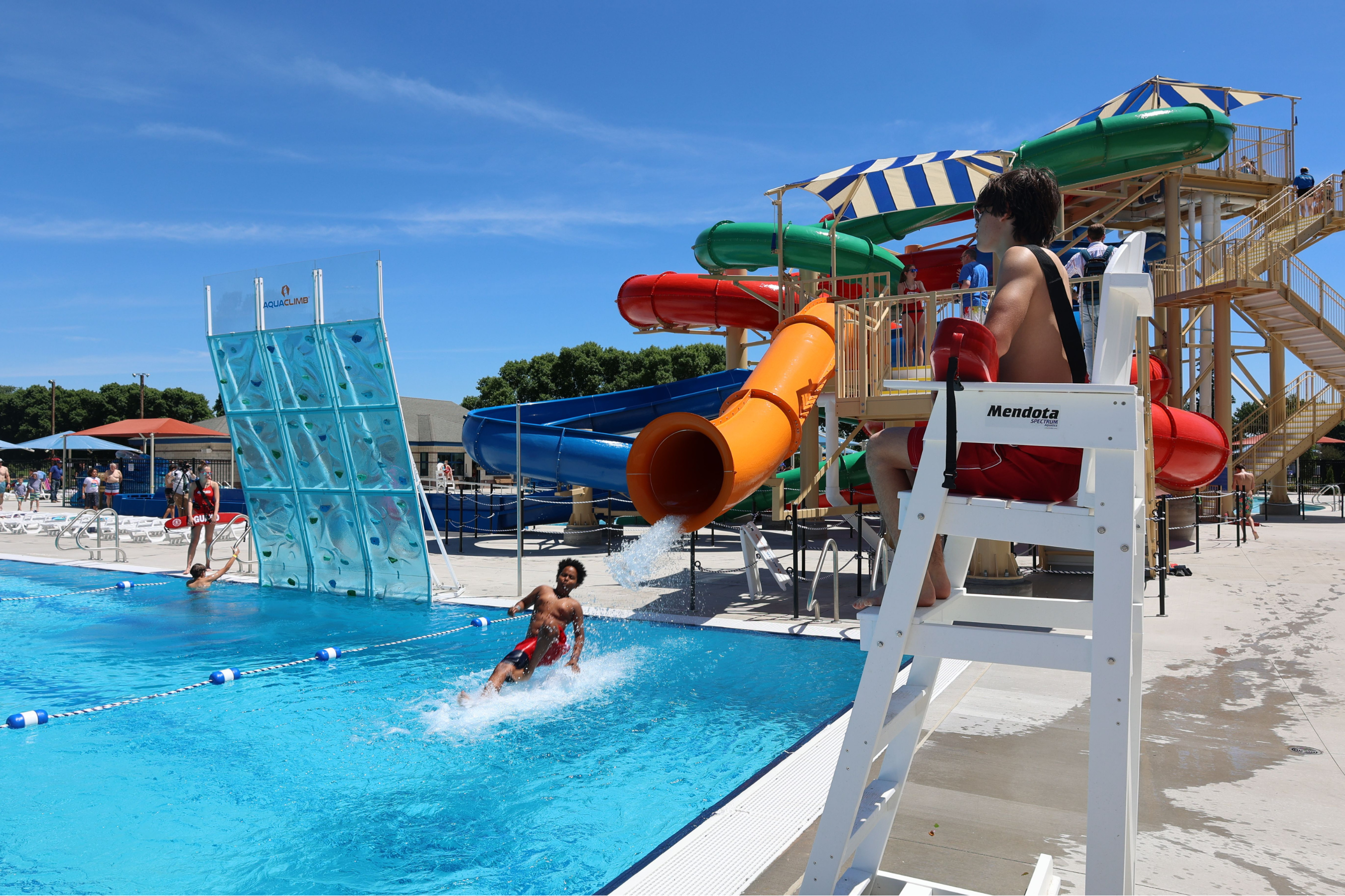 a person coming out a water slide into a pool adjacent to a climbing wall