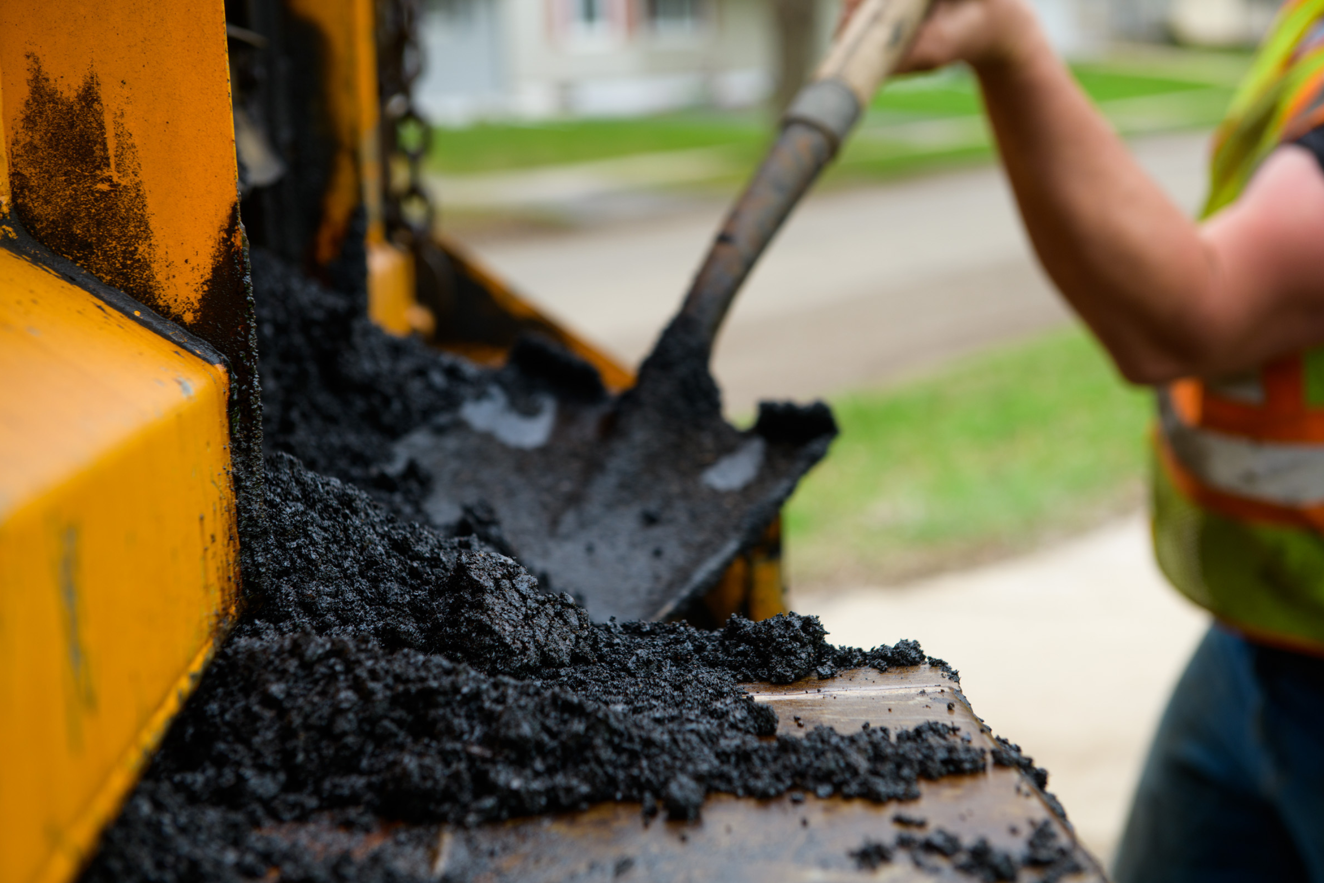 a shovel moving asphalt out of a truck near a street construction site