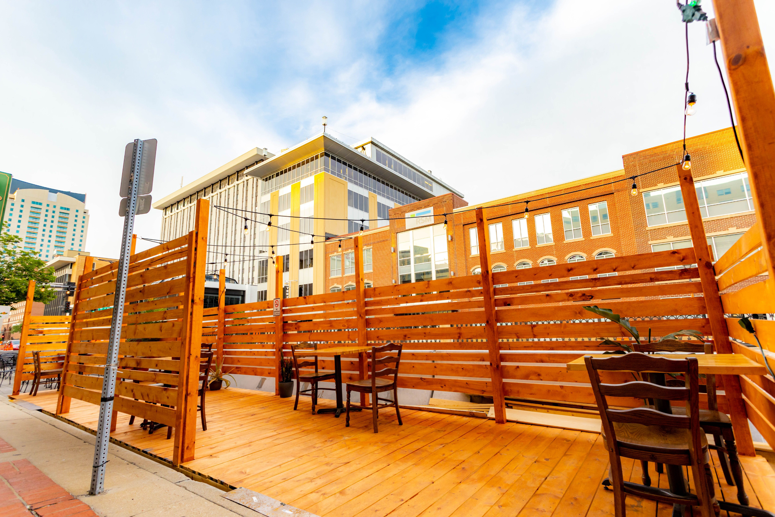 A temporary cafe built on the street with tables and chairs and a wooden fence