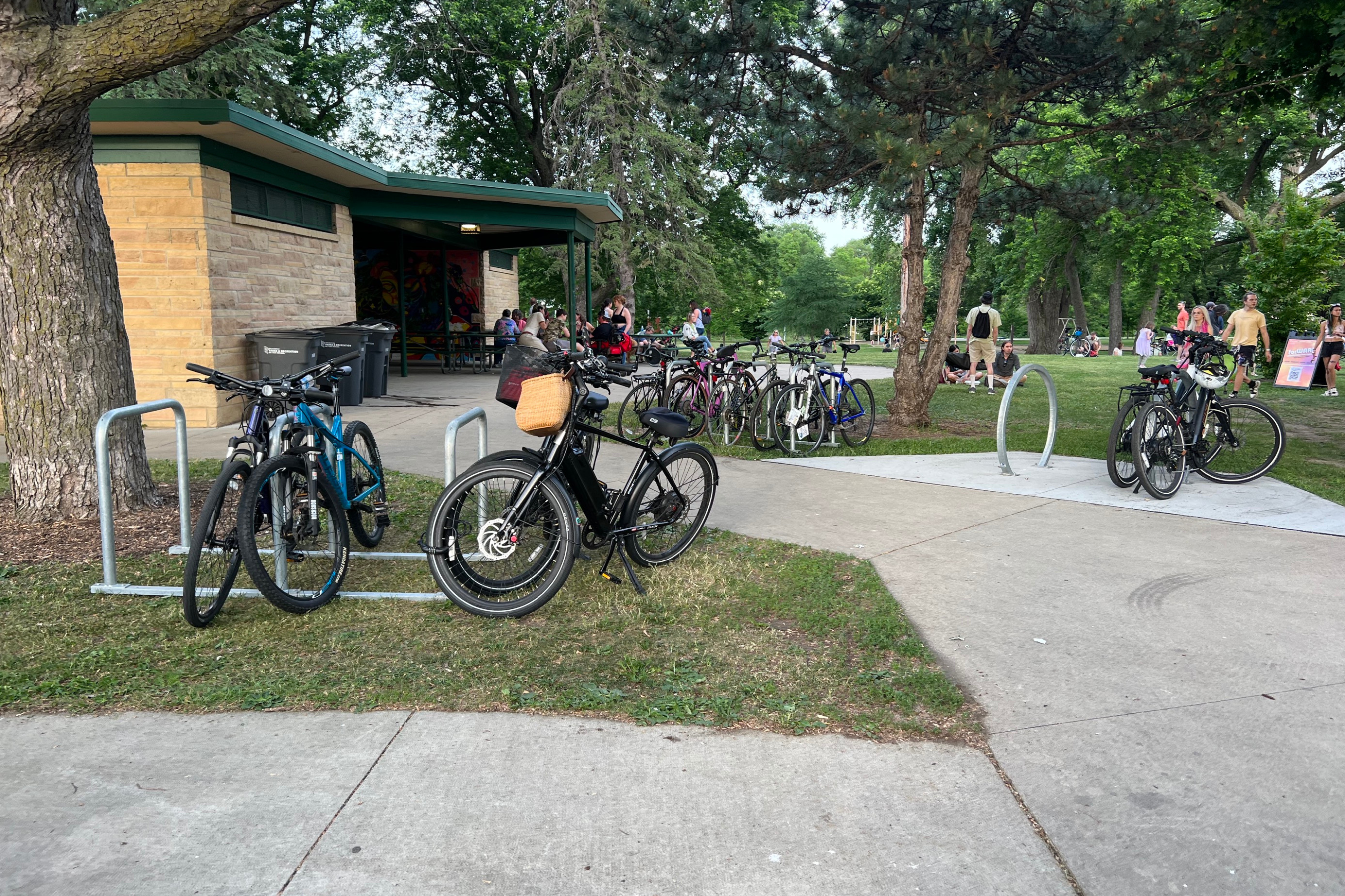 about a dozen bikes parked at bike racks at a busy park in summer