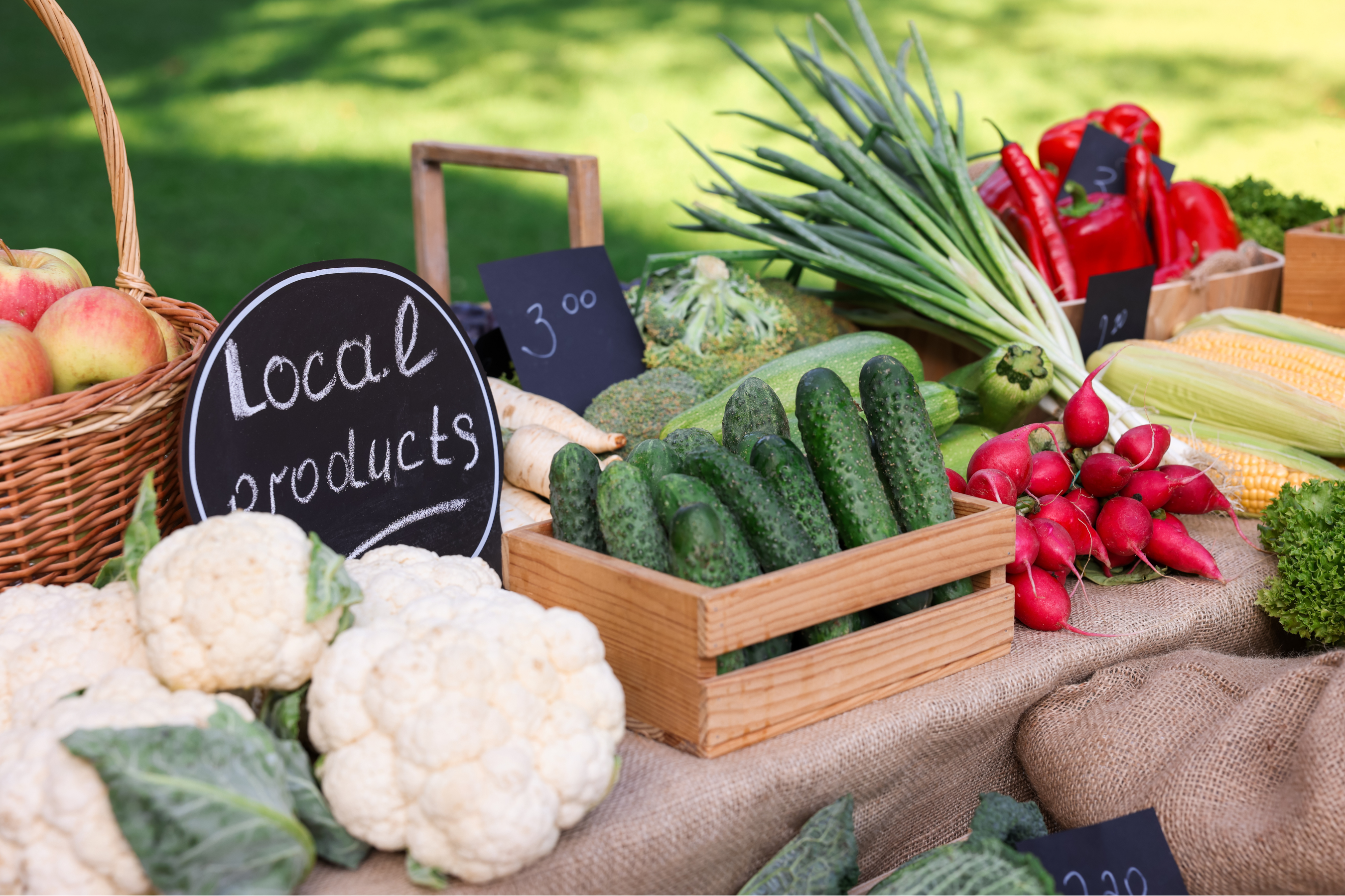 a market stand with various fresh produce including cucumbers, cauliflower, apples, radishes and more