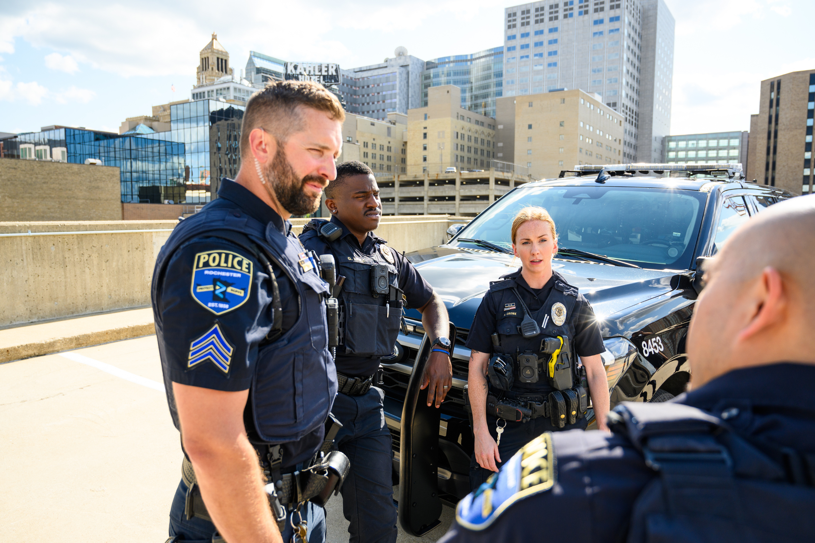 multiple police offers interacting with each other in front of a squad car on the top of a parking garage