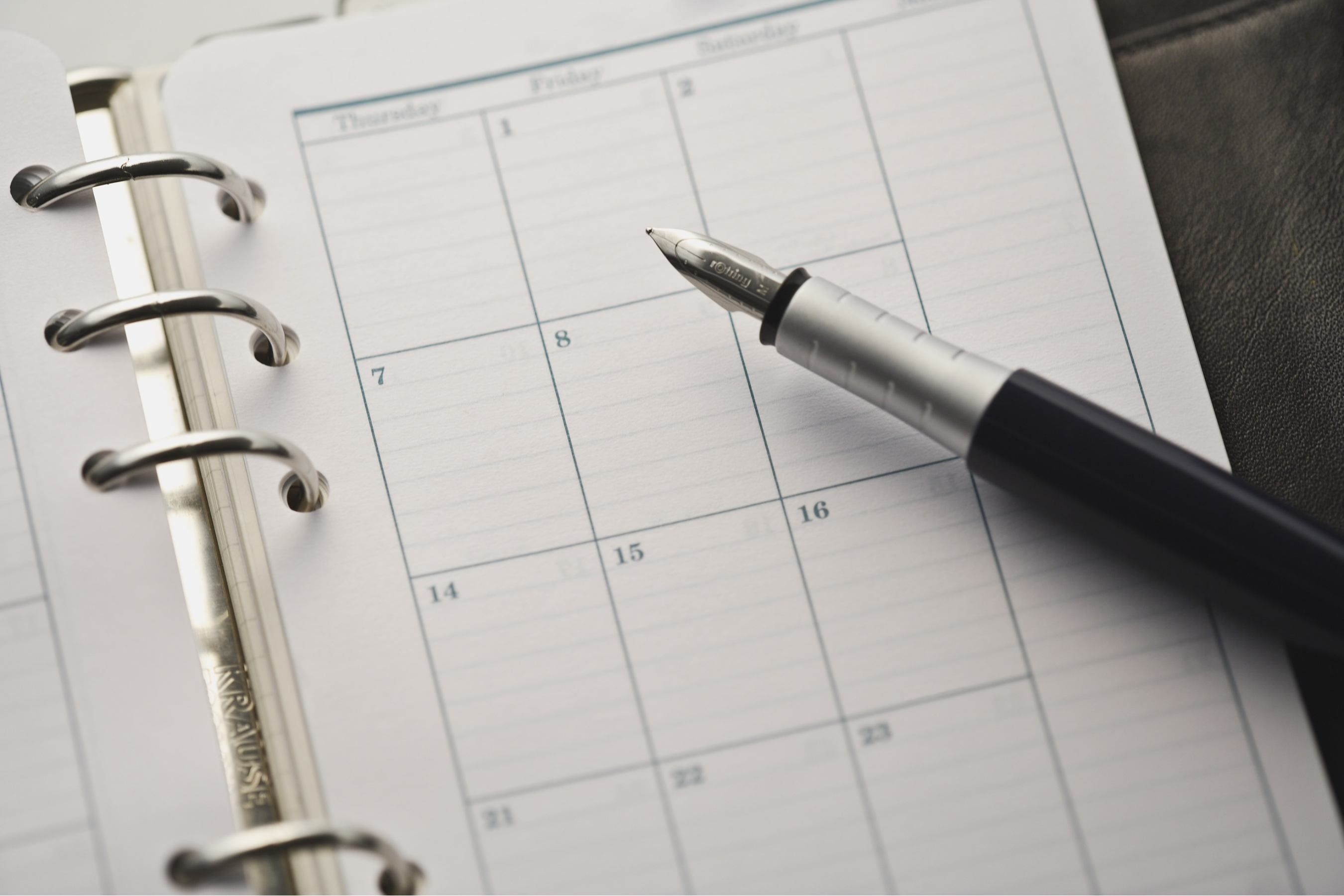 a pen resting on a calendar planner spiral notebook