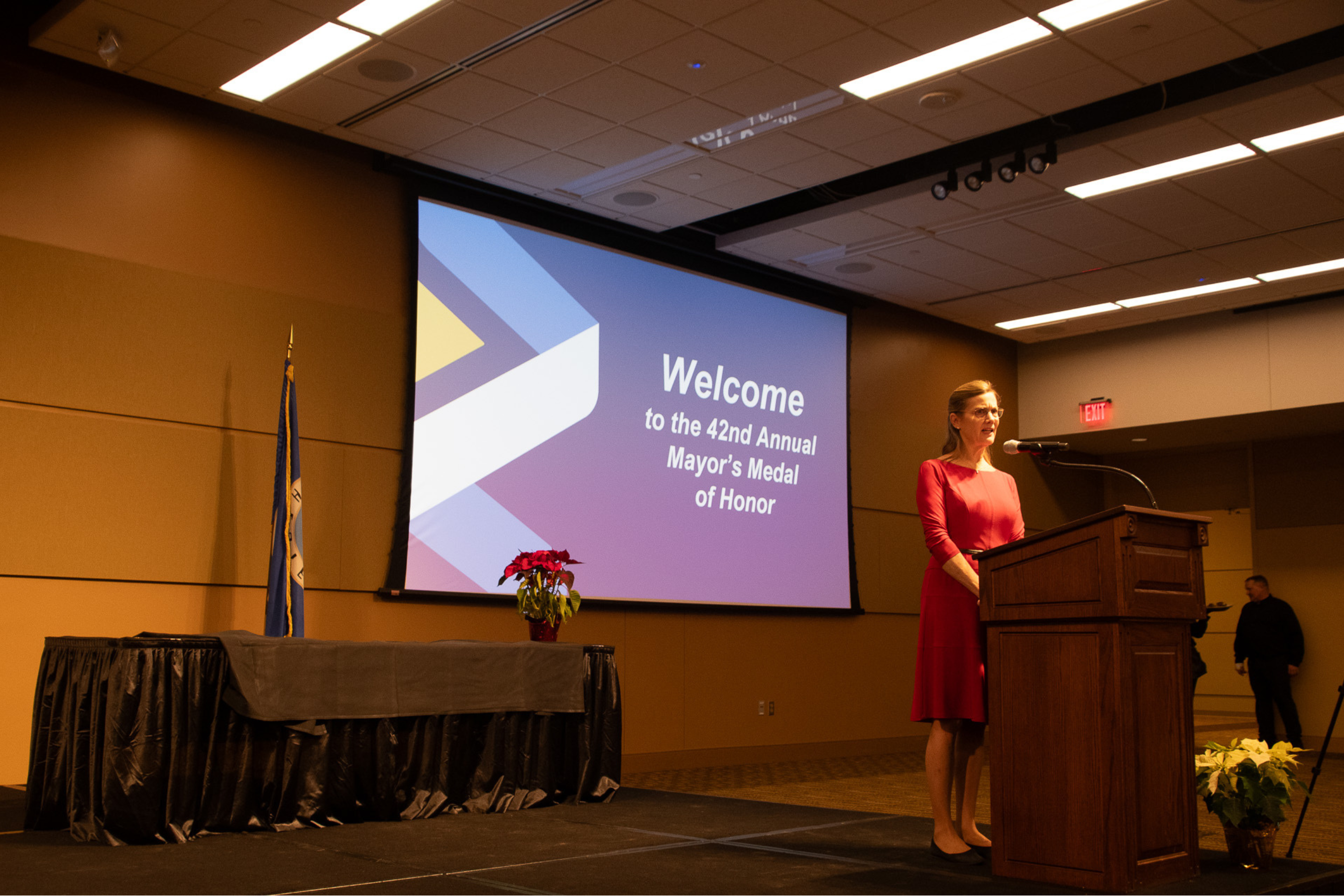 Mayor Kim Norton standing on a stage at a podium presenting the Mayor's Medal of Honor