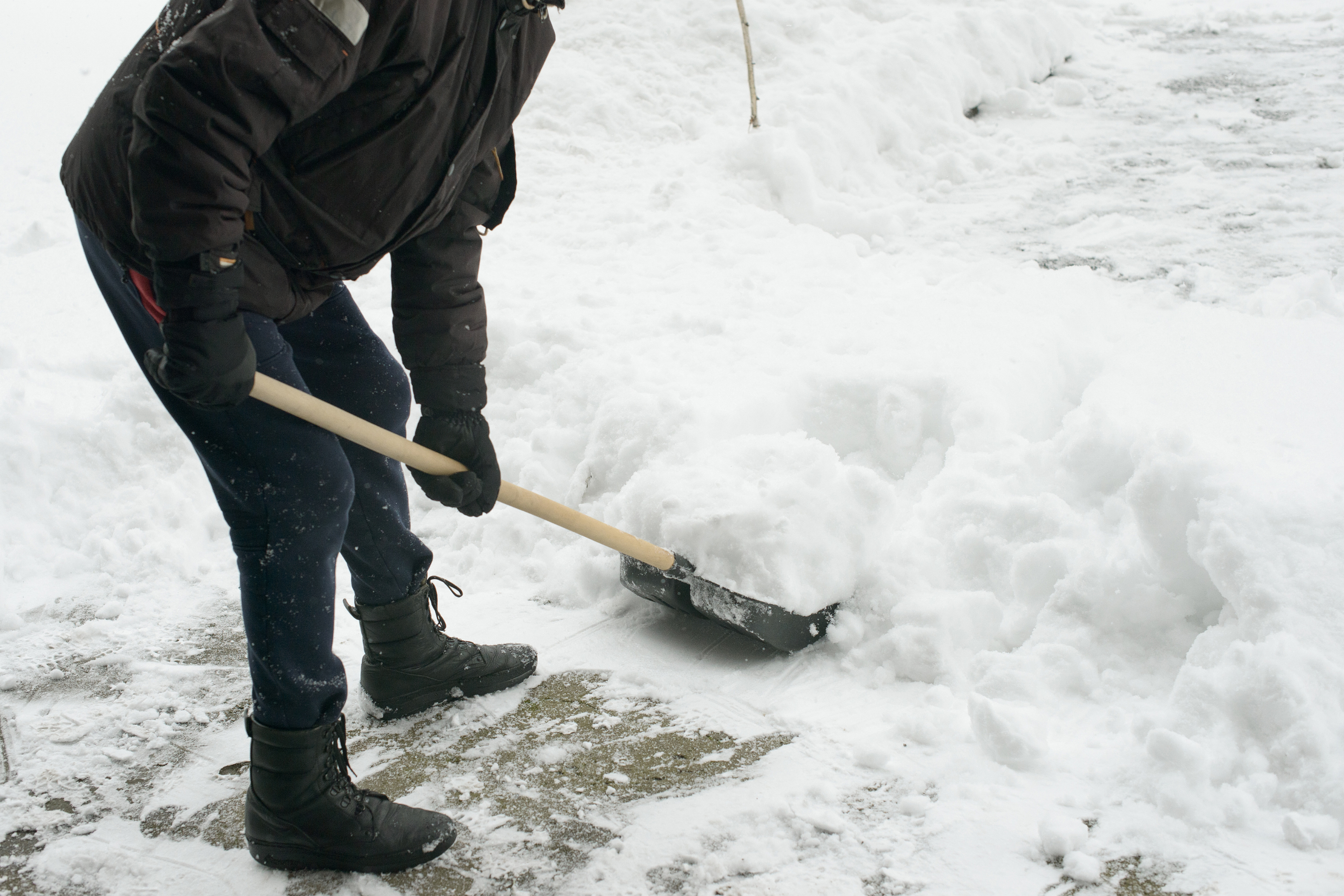 an unidentifiable person shoveling snow on a sidewalk