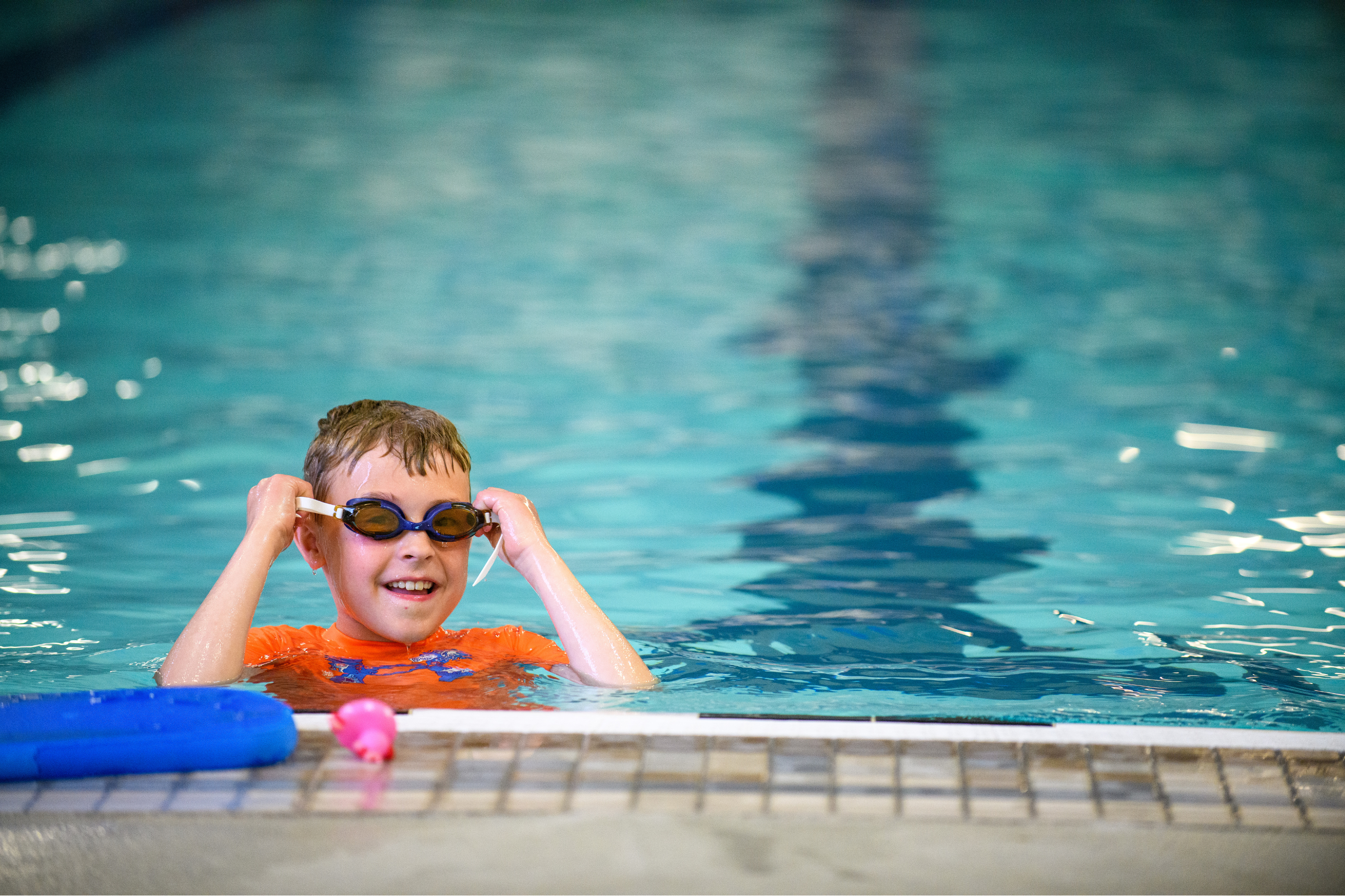 a young boy at the edge of a pool putting goggles on and smiling