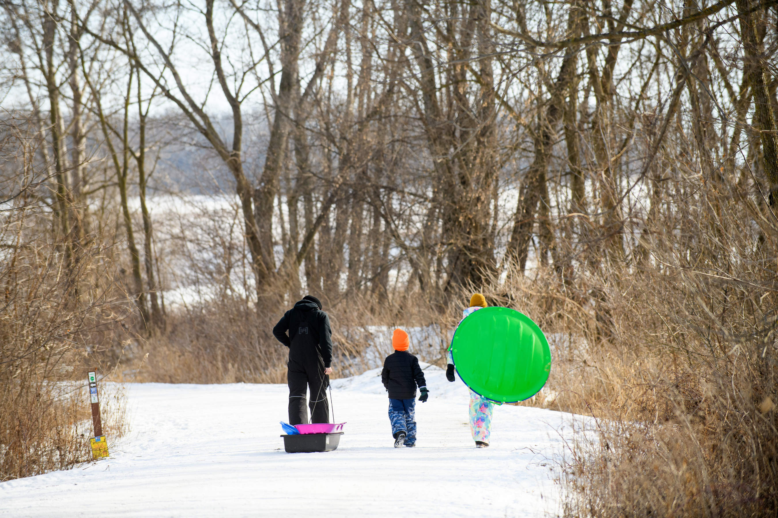an two adults and a child pulling and carrying sleds on a snowy trail