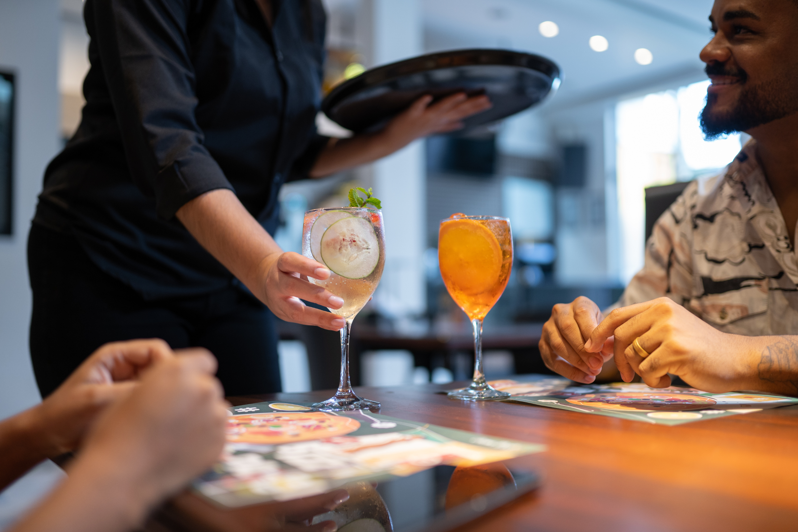 a server delivering two drinks to people seated at a table