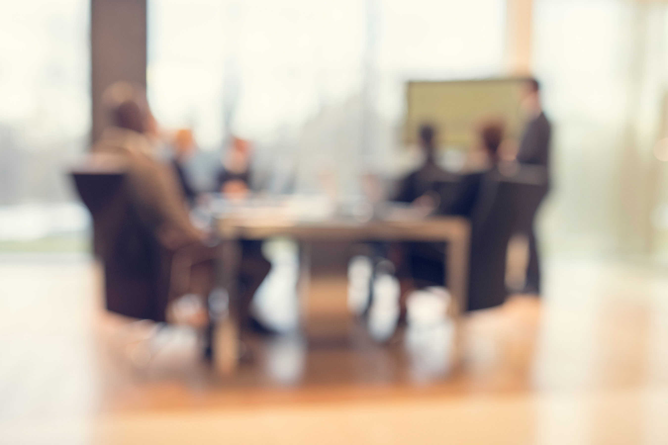 an out-of-focus view of a board room with multiple people seated at a table
