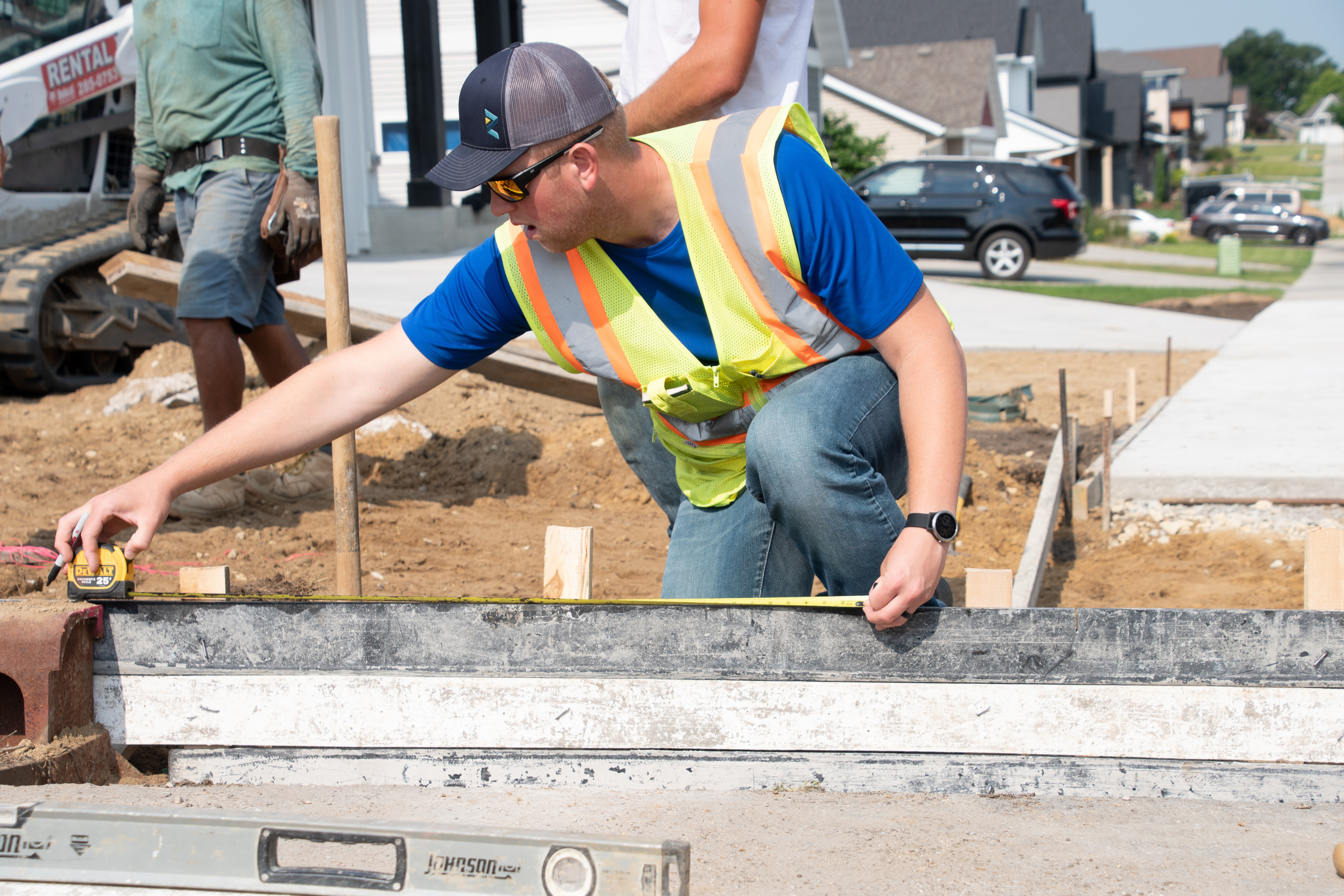 a person wearing a construction vest, measuring something on the ground in the middle of a construction site