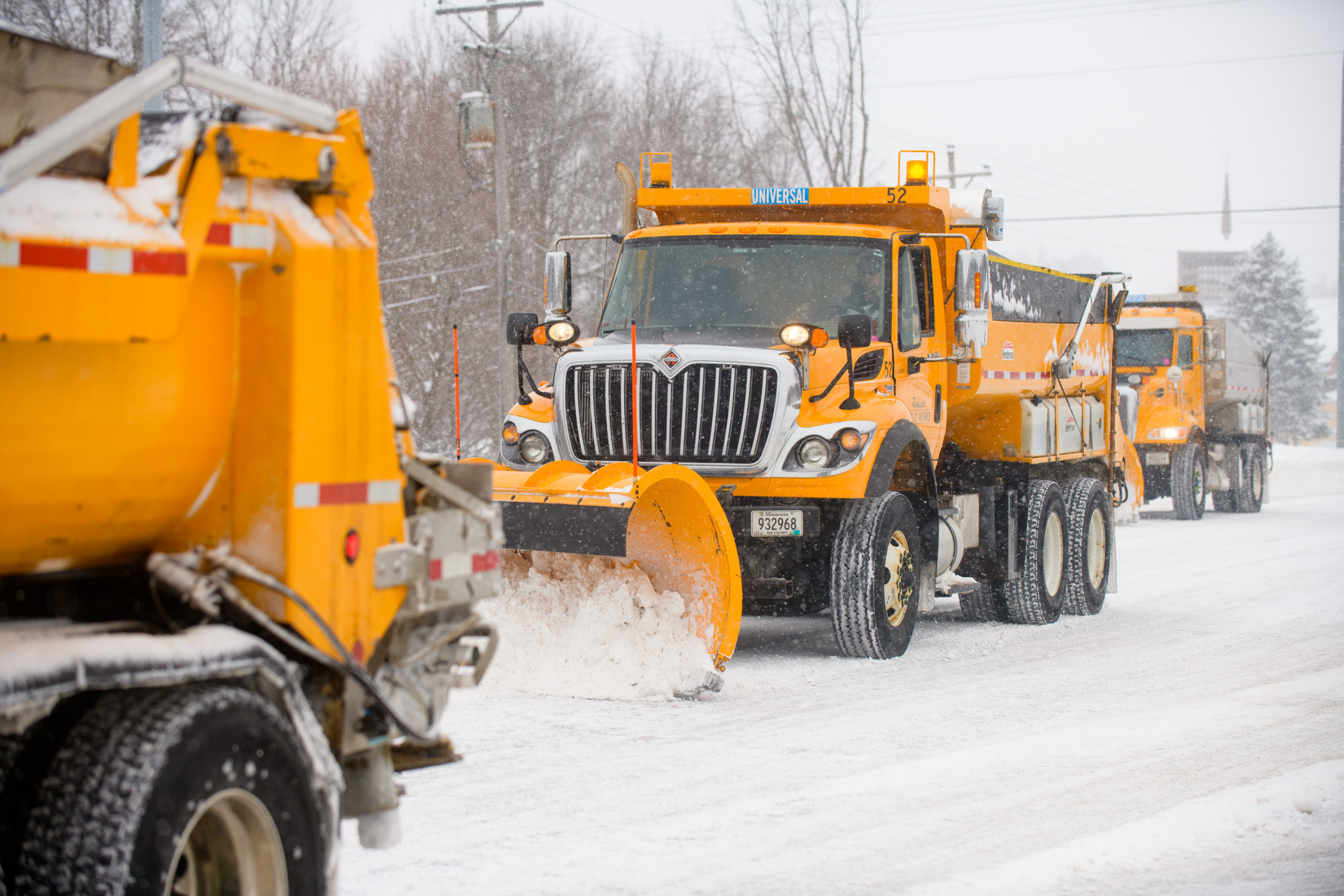 three snow plow trucks operating in a line on a snowy roadway
