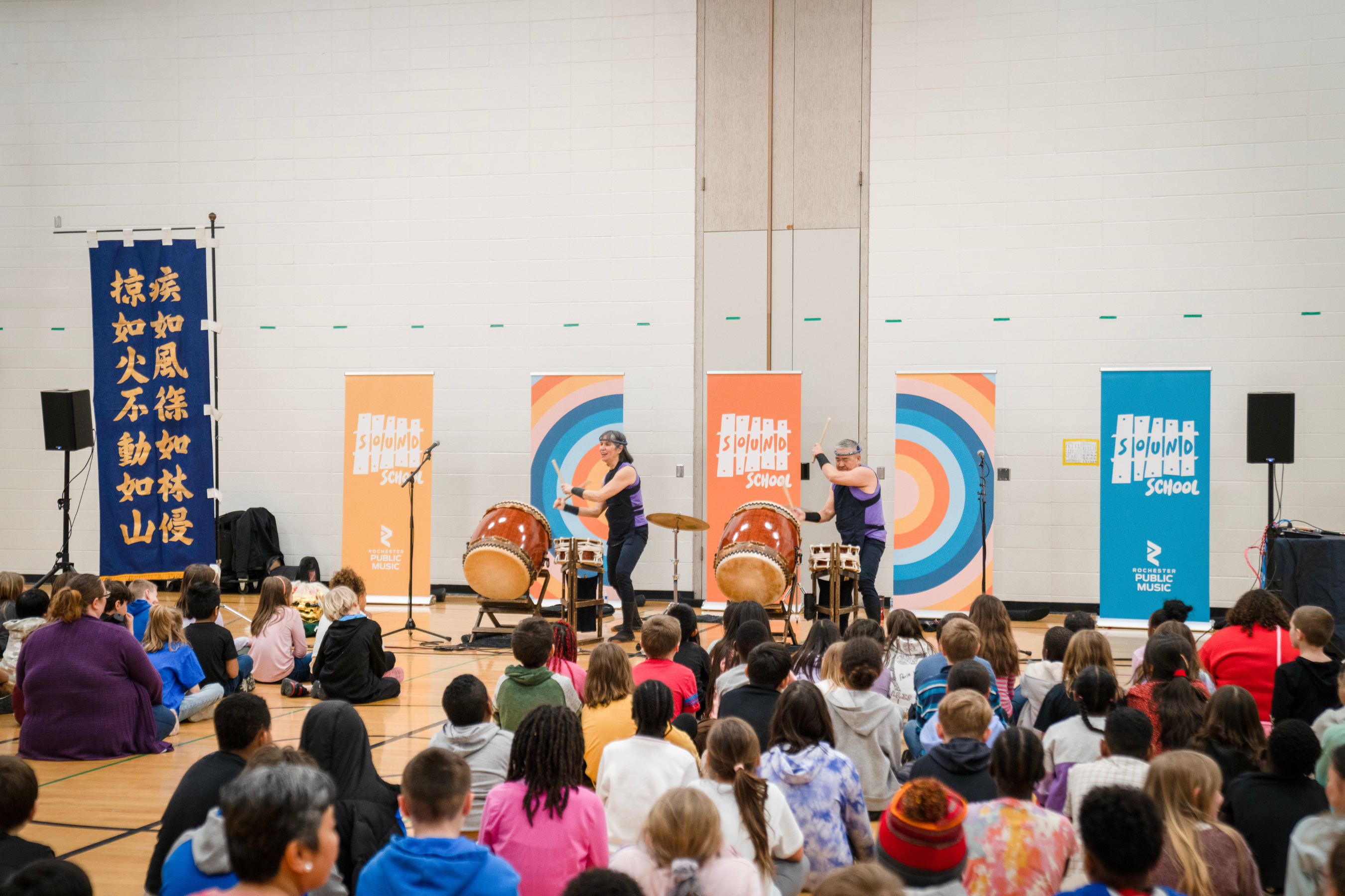 two performers playing drums to a crowd of school-aged children
