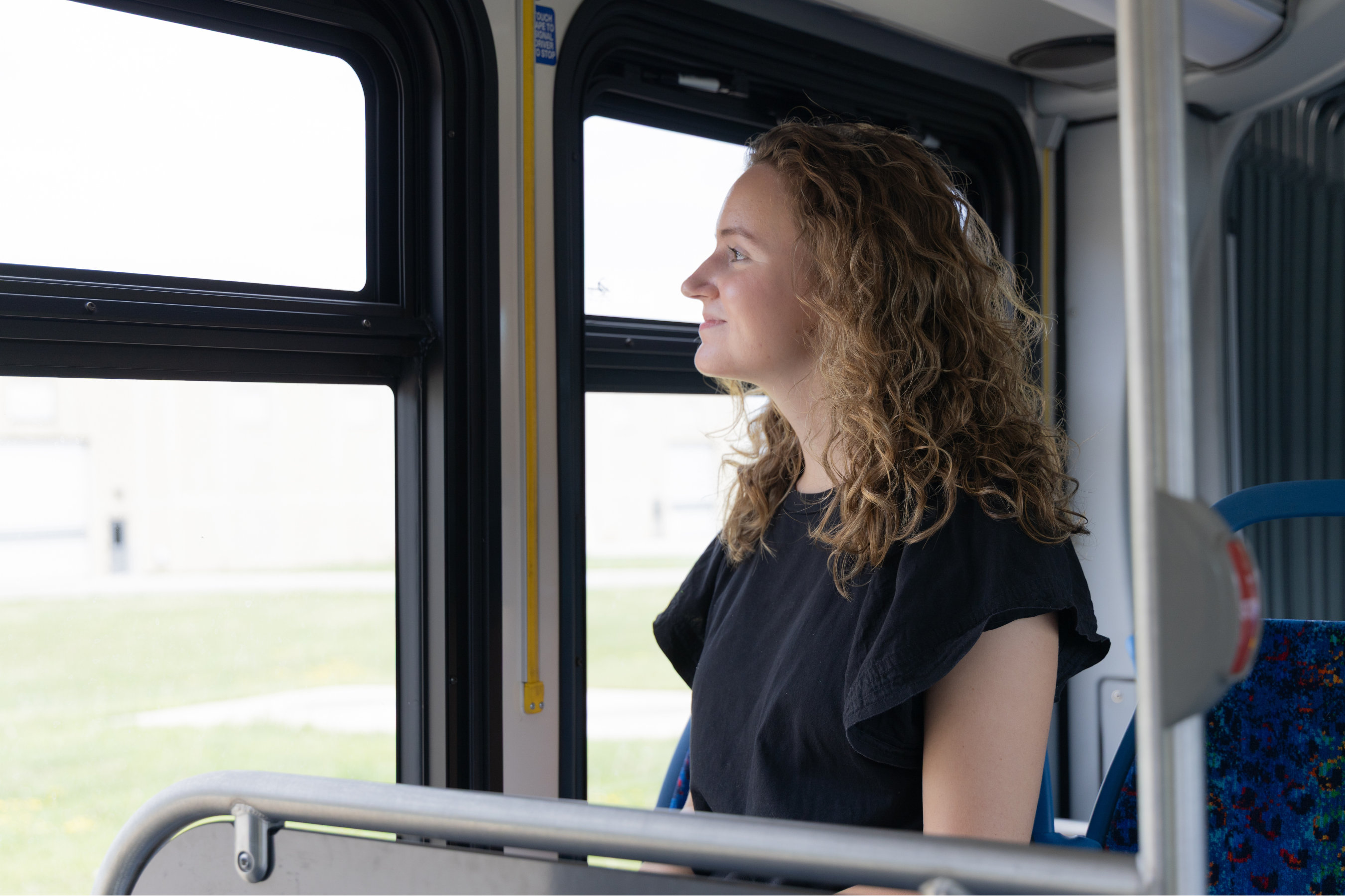 a young woman riding a city bus and looking out the window while smiling