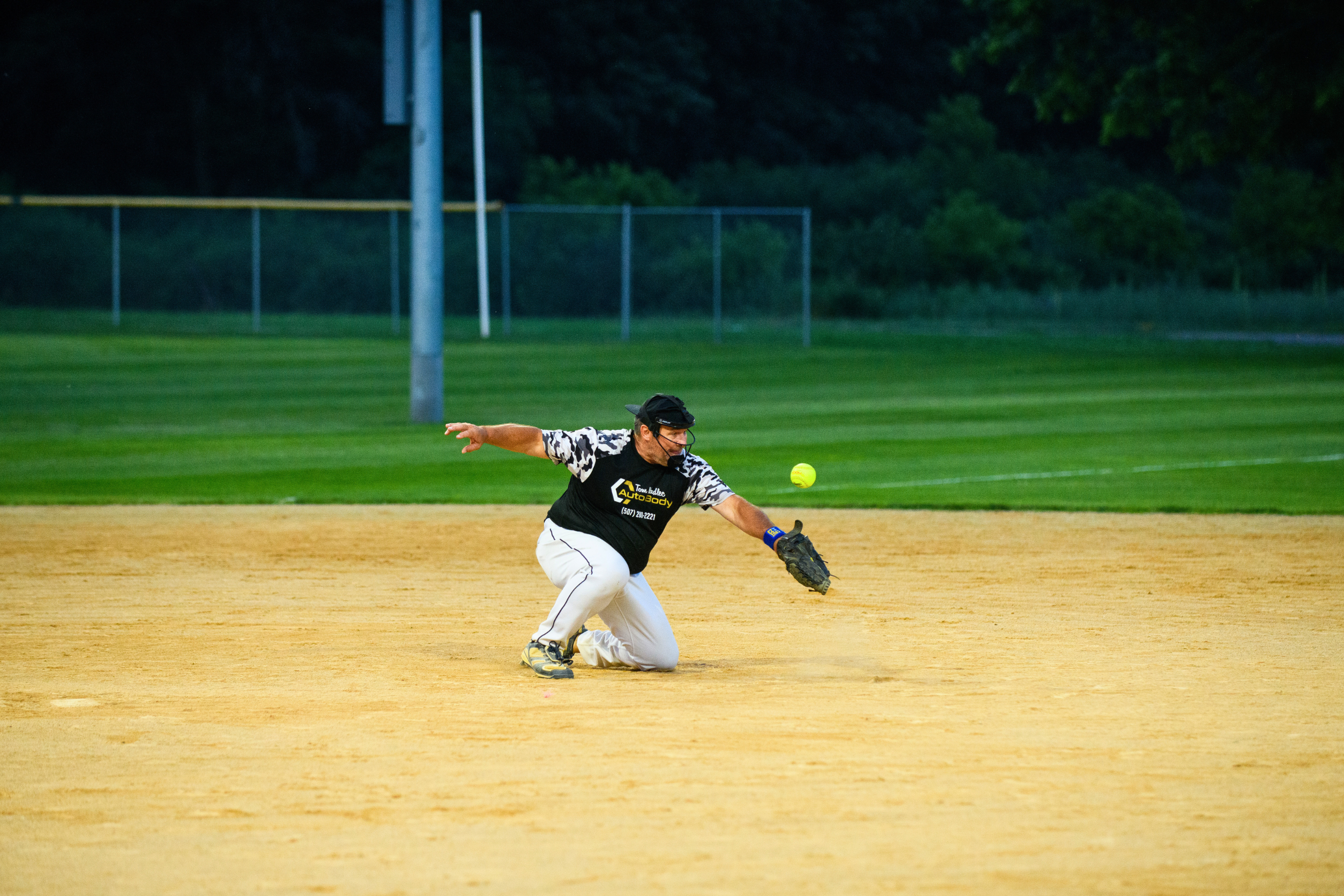 a male softball player kneeling in the dirt to catch a low ball
