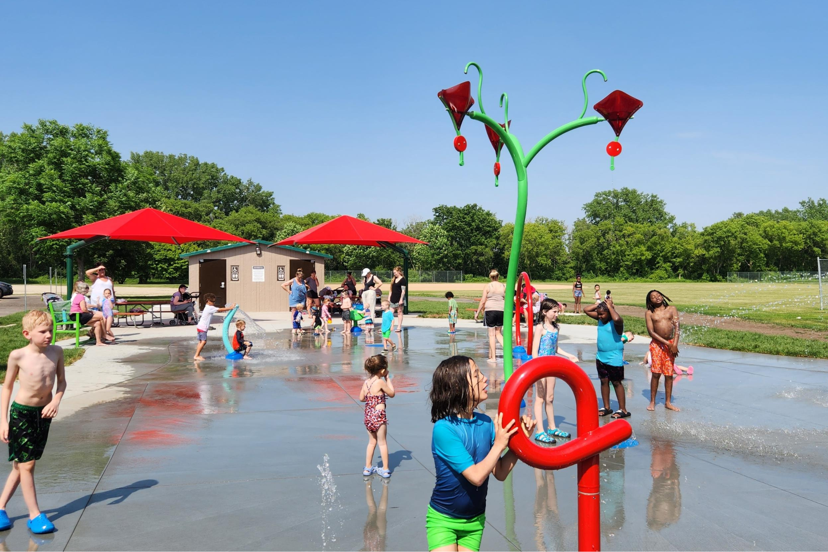 people of all ages enjoying a splash pad in the middle of a park on a summer day