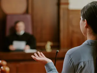 a person testifying in a courtroom, seen from behind, with a judge blurred in the background