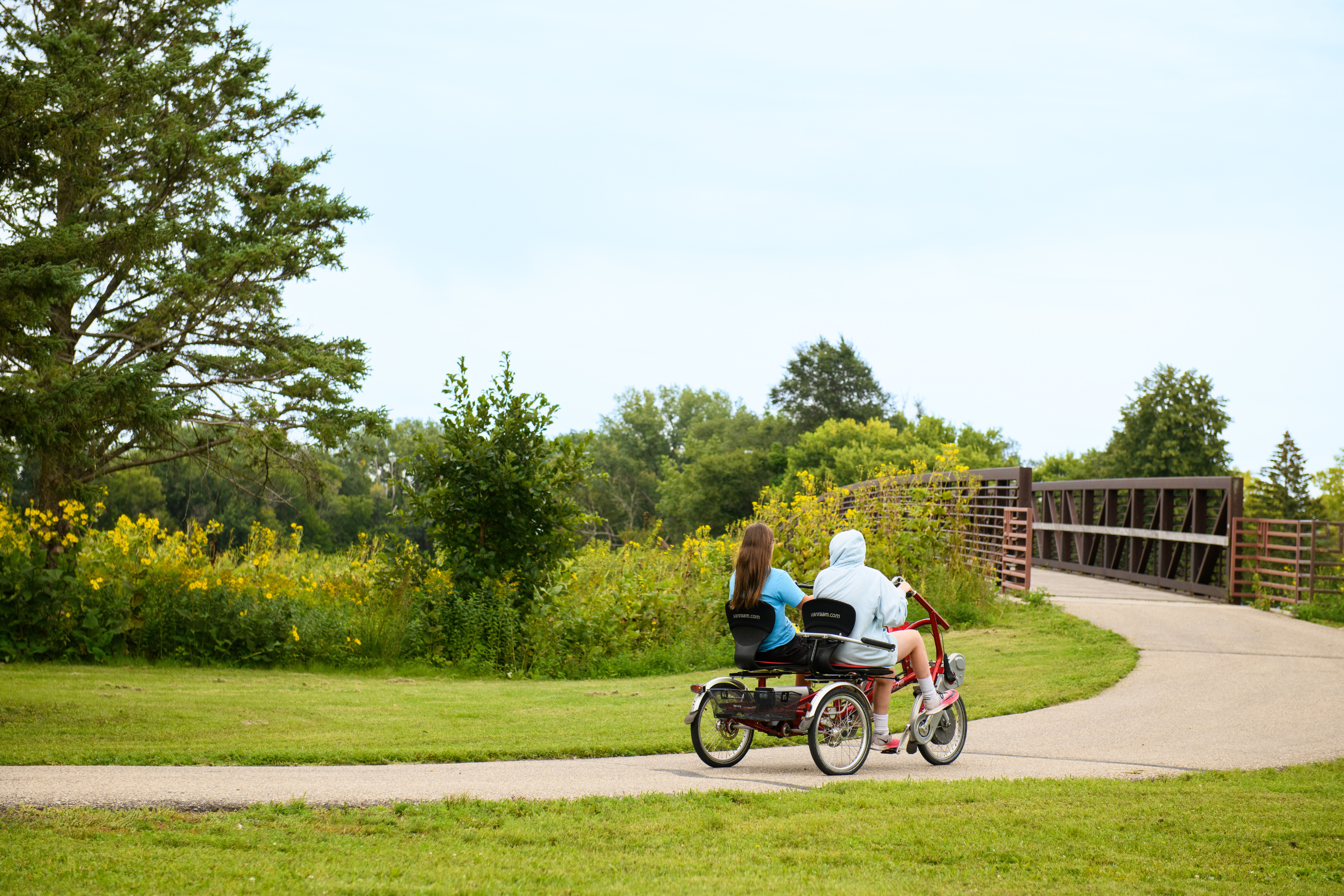 two people on an adaptive bike riding on a trail in the summer