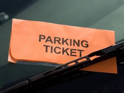 a bright orange paper that reads 'parking ticket' tucked under a wiper blade