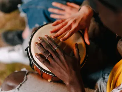 two hands of different races playing one drum positioned between a person's knees