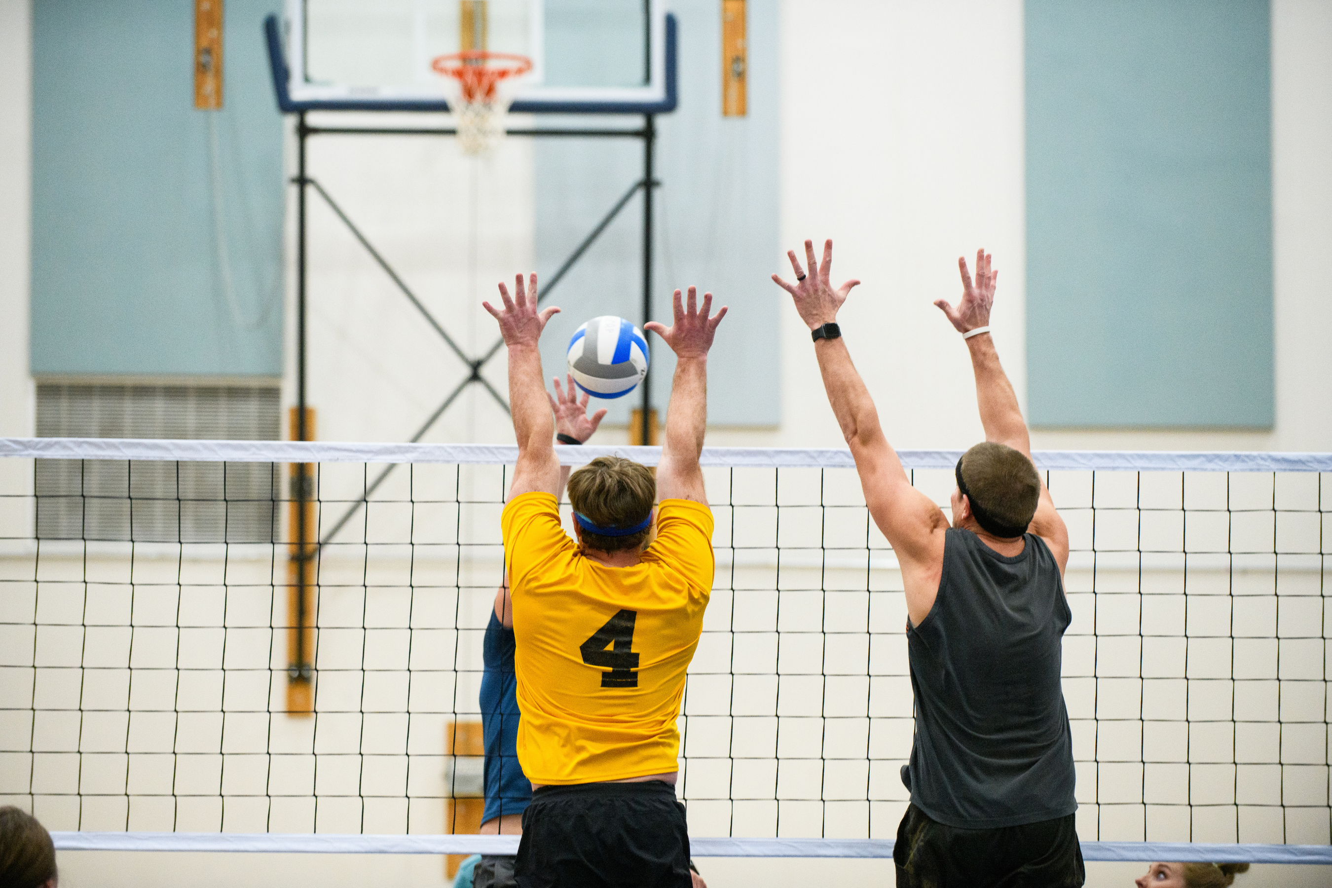 two men jumping to block a volleyball at an indoor net