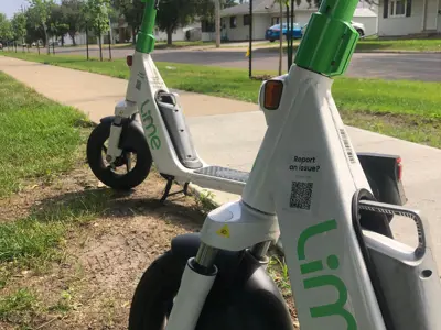 Two Lime scooters parked by sidewalk