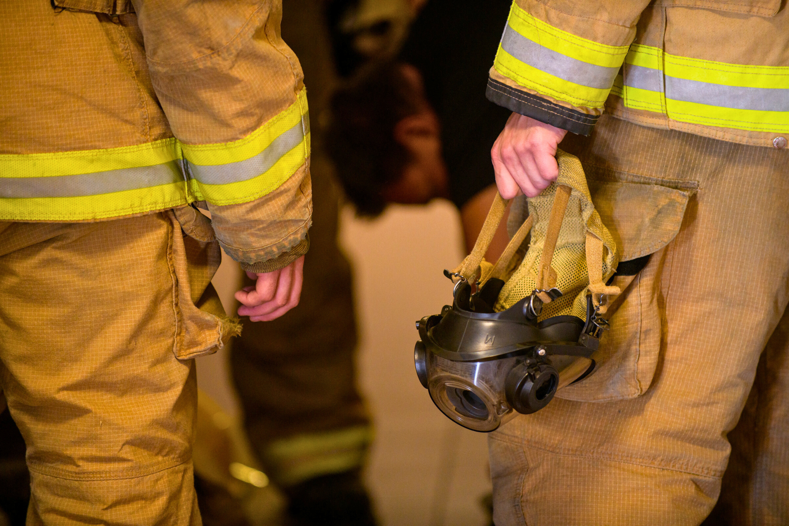 close up view of two firefighters hands, one holding a gas mask