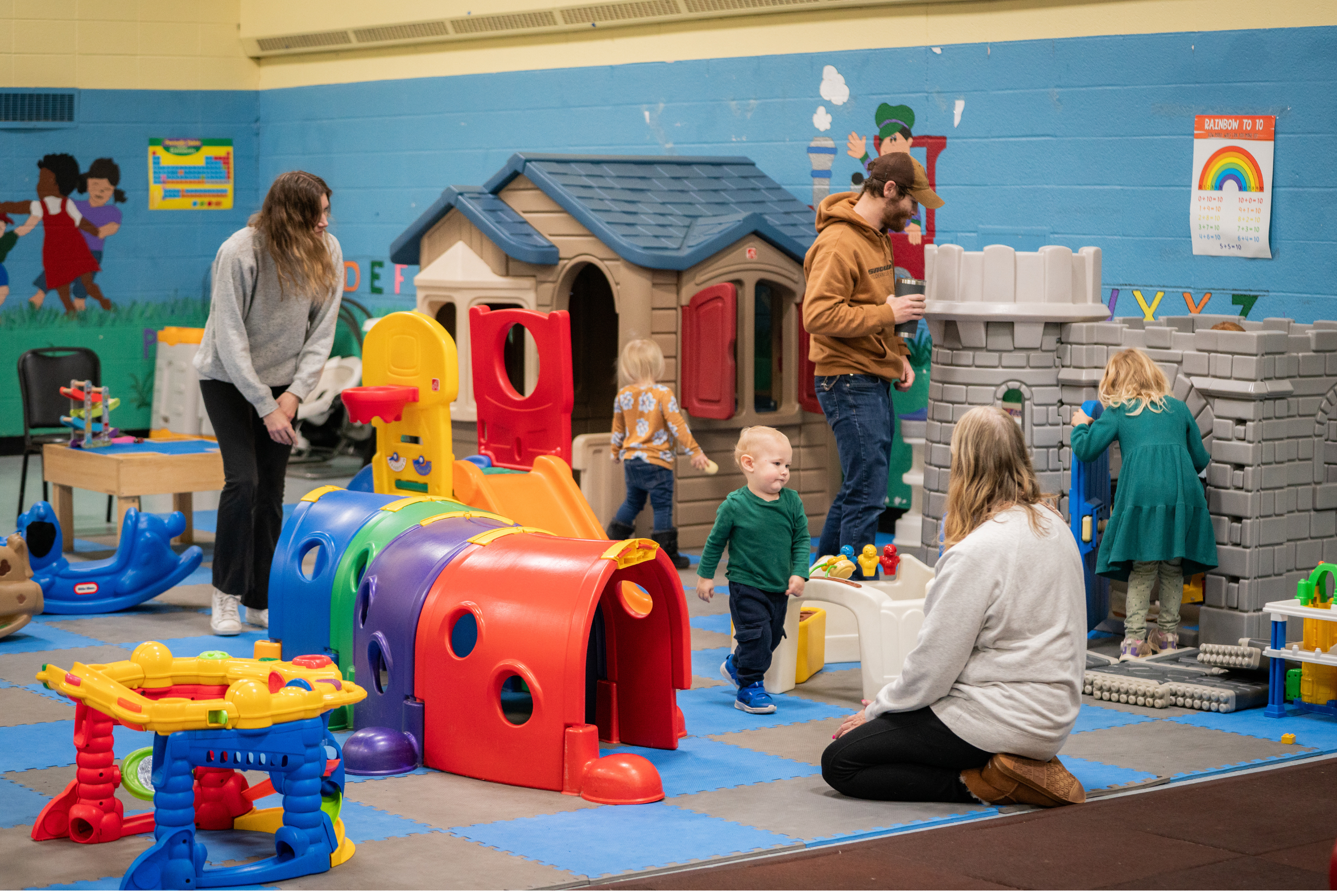 children playing at an indoor playground while being supervised by adults