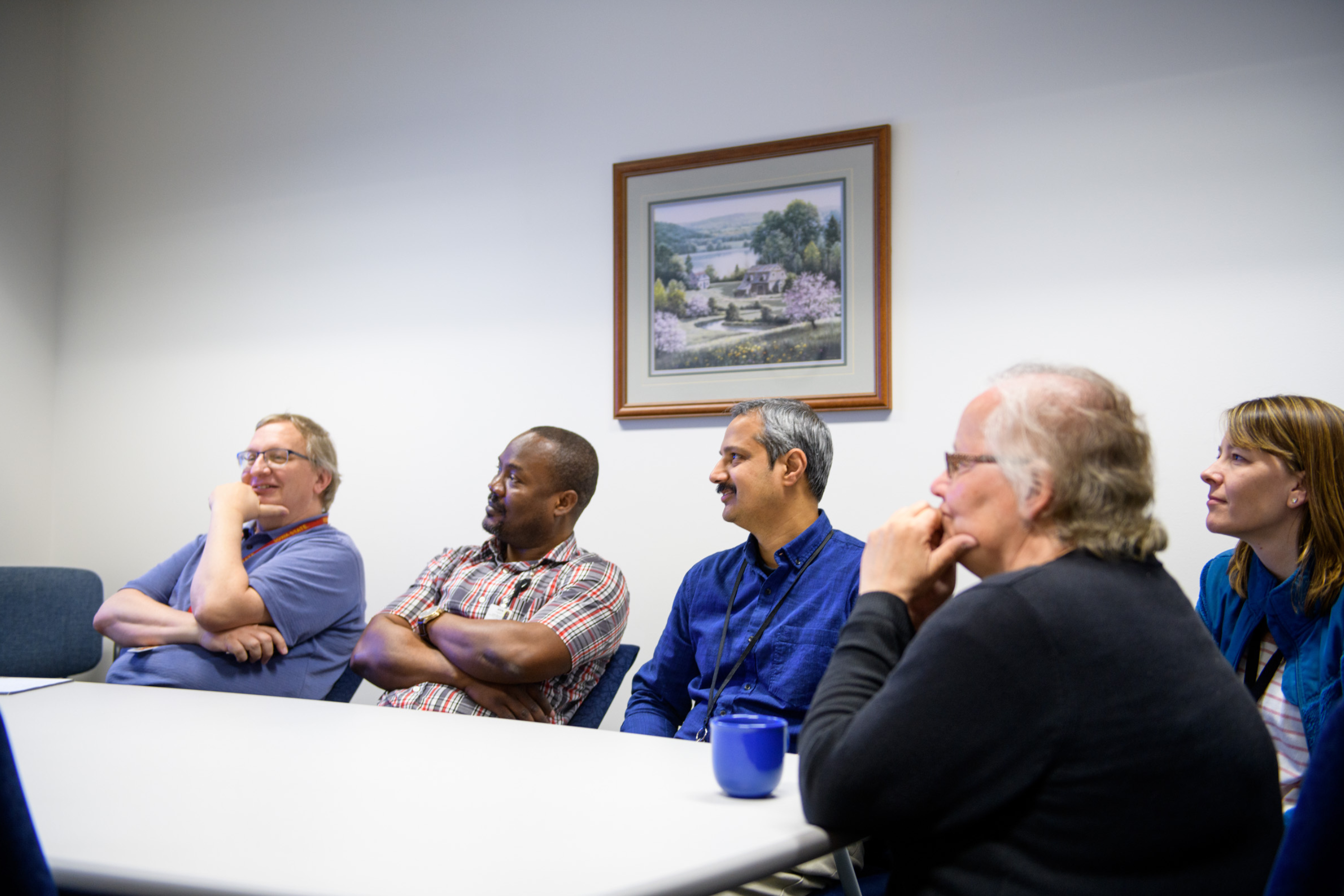 several people sitting at a meeting table looking at something off screen and smiling
