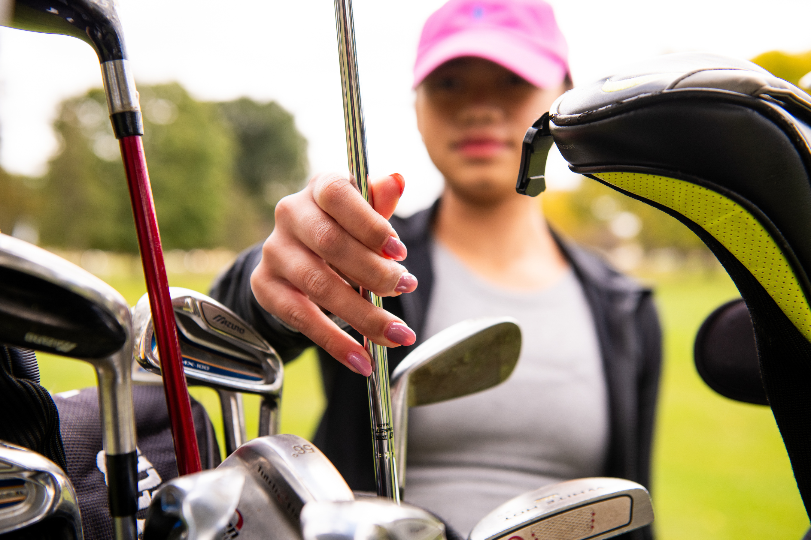 An out of focus woman grabbing a golf club out of a golf bag