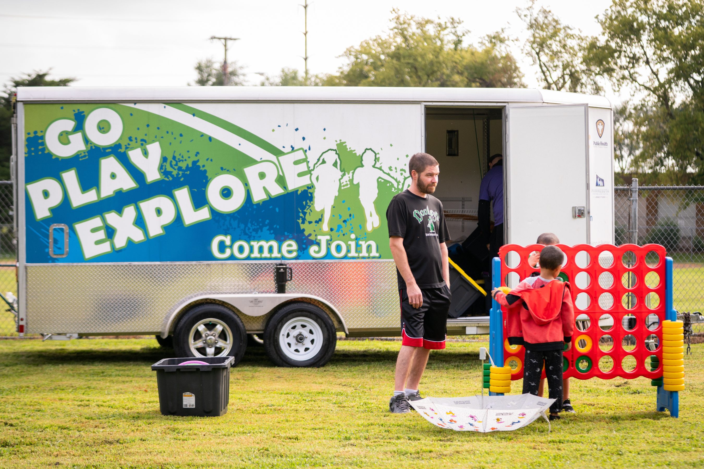 a child and adult playing yard games in front of the 'Go Play Explore' Mobile Recreation trailer