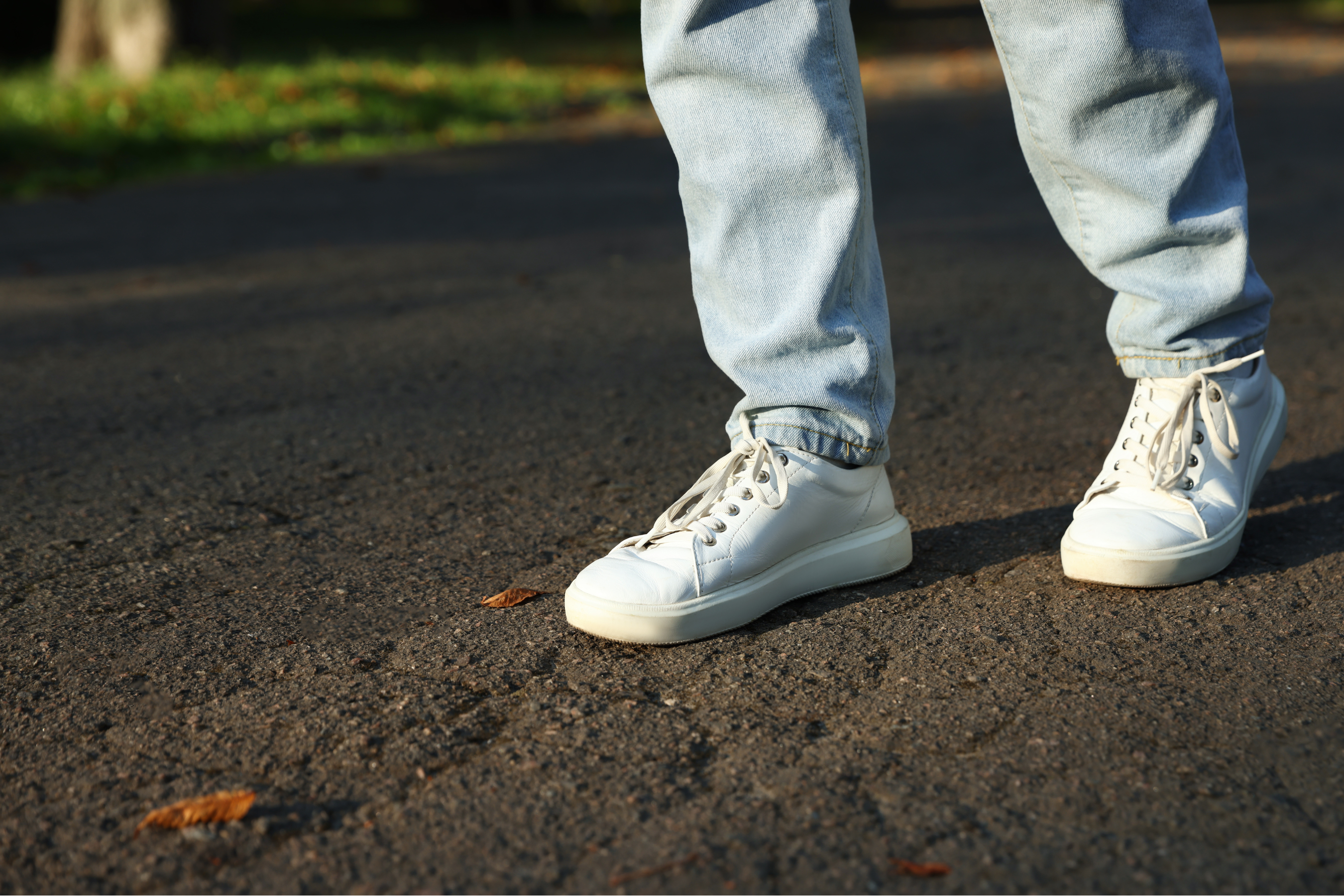 a pair of feet wearing white tennis shoes walking on a paved outdoor surface