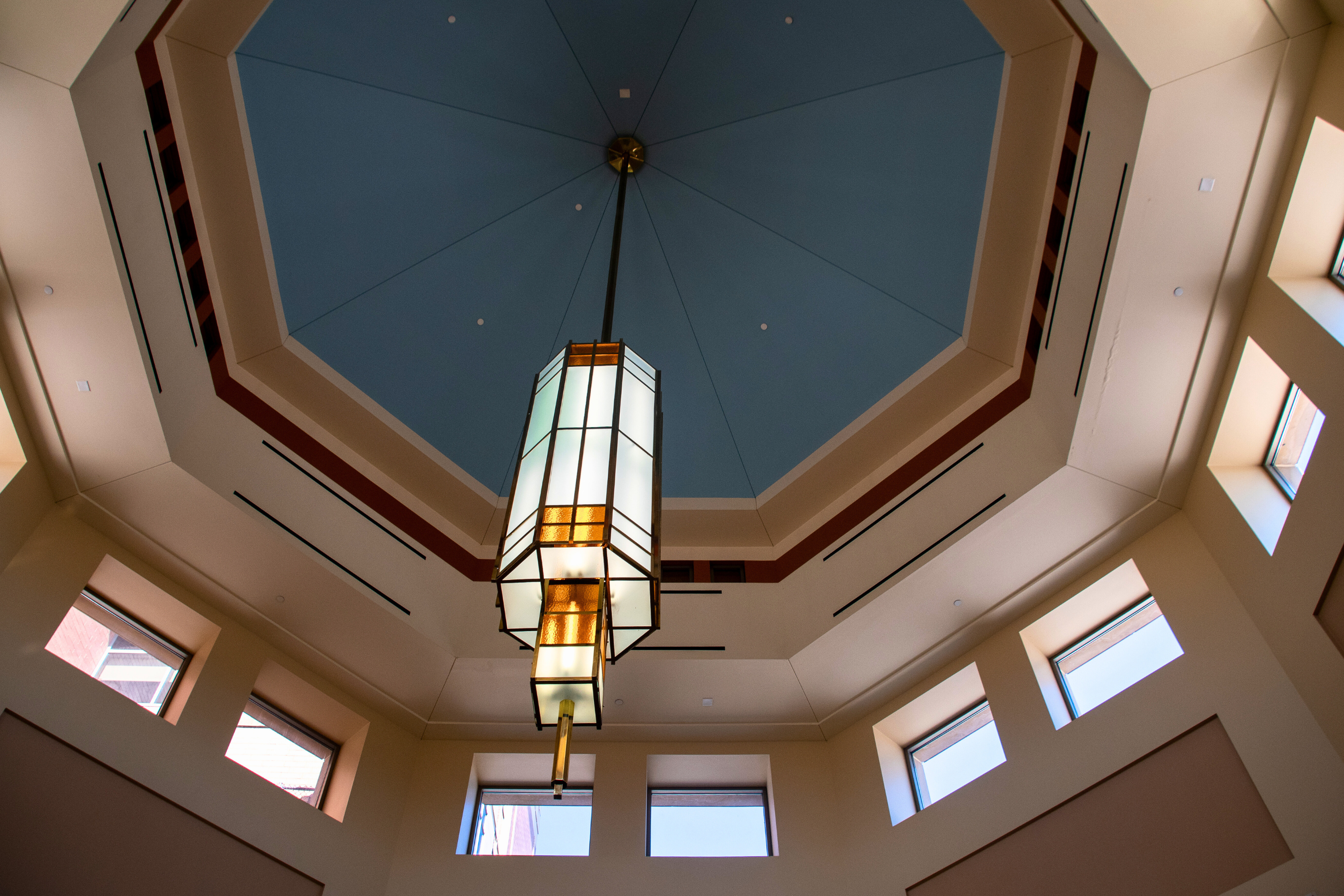 A glass light fixture hanging from a blue ceiling in a city hall atrium