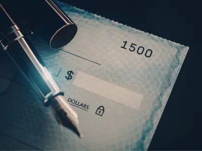 a blank check on a dark background with an old-fashioned pen resting on top