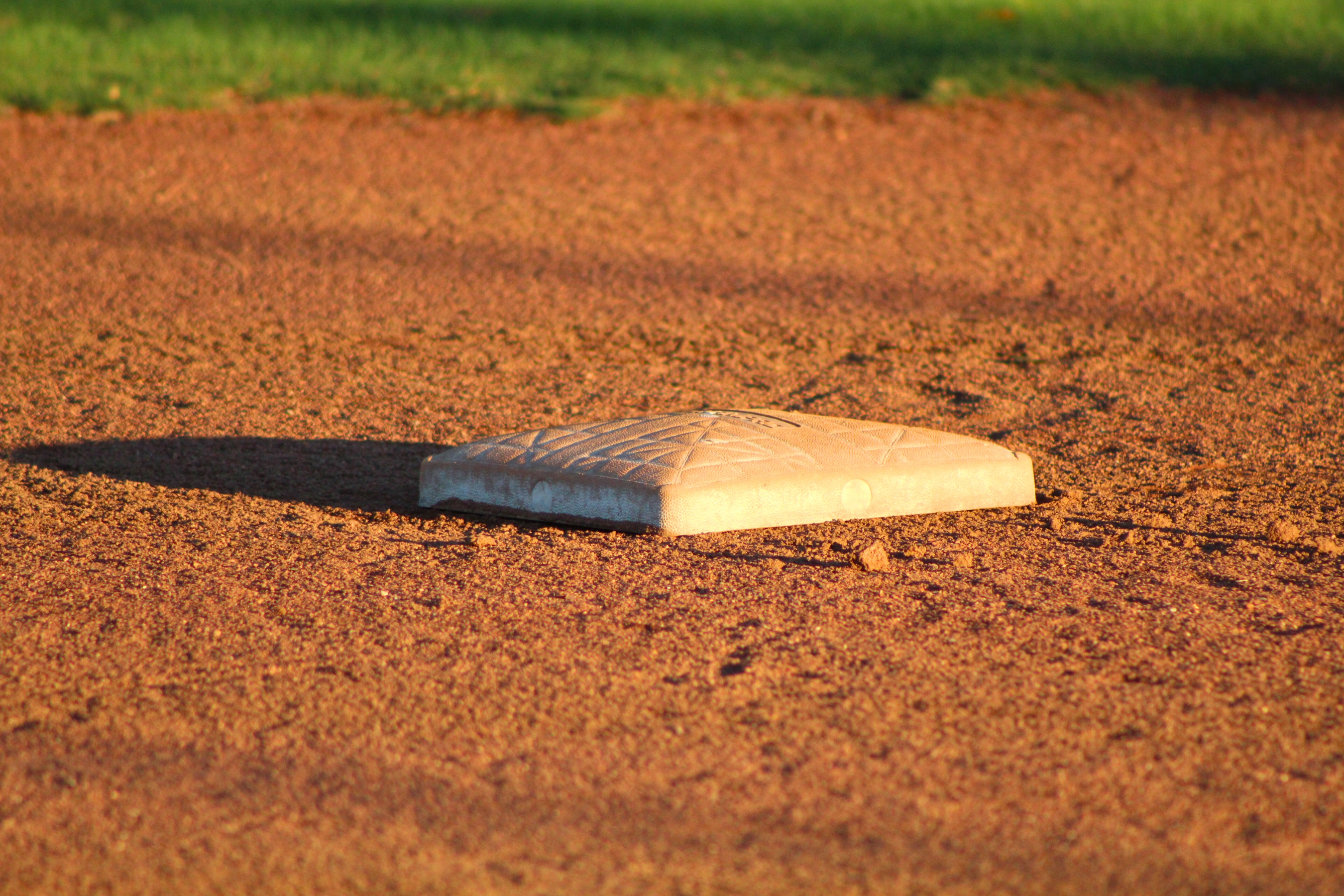 close up view of a base on the dirt of a baseball diamond with grass in the background