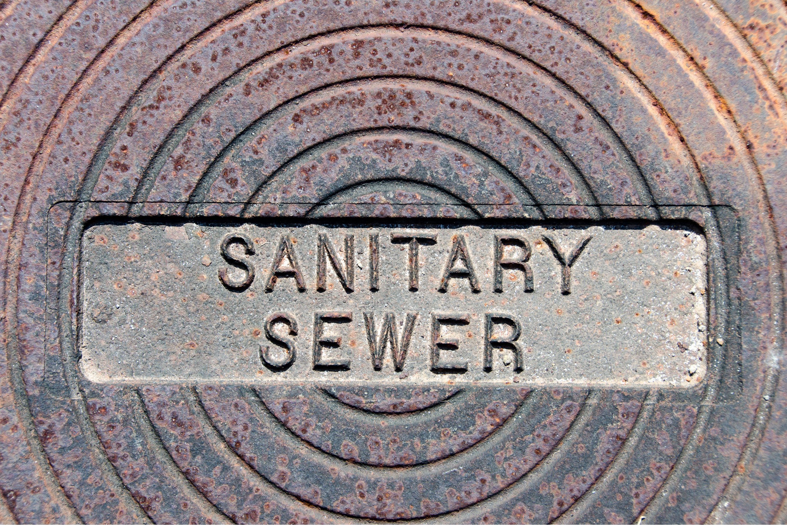 a rusted manhole cover with the words 'sanitary sewer'