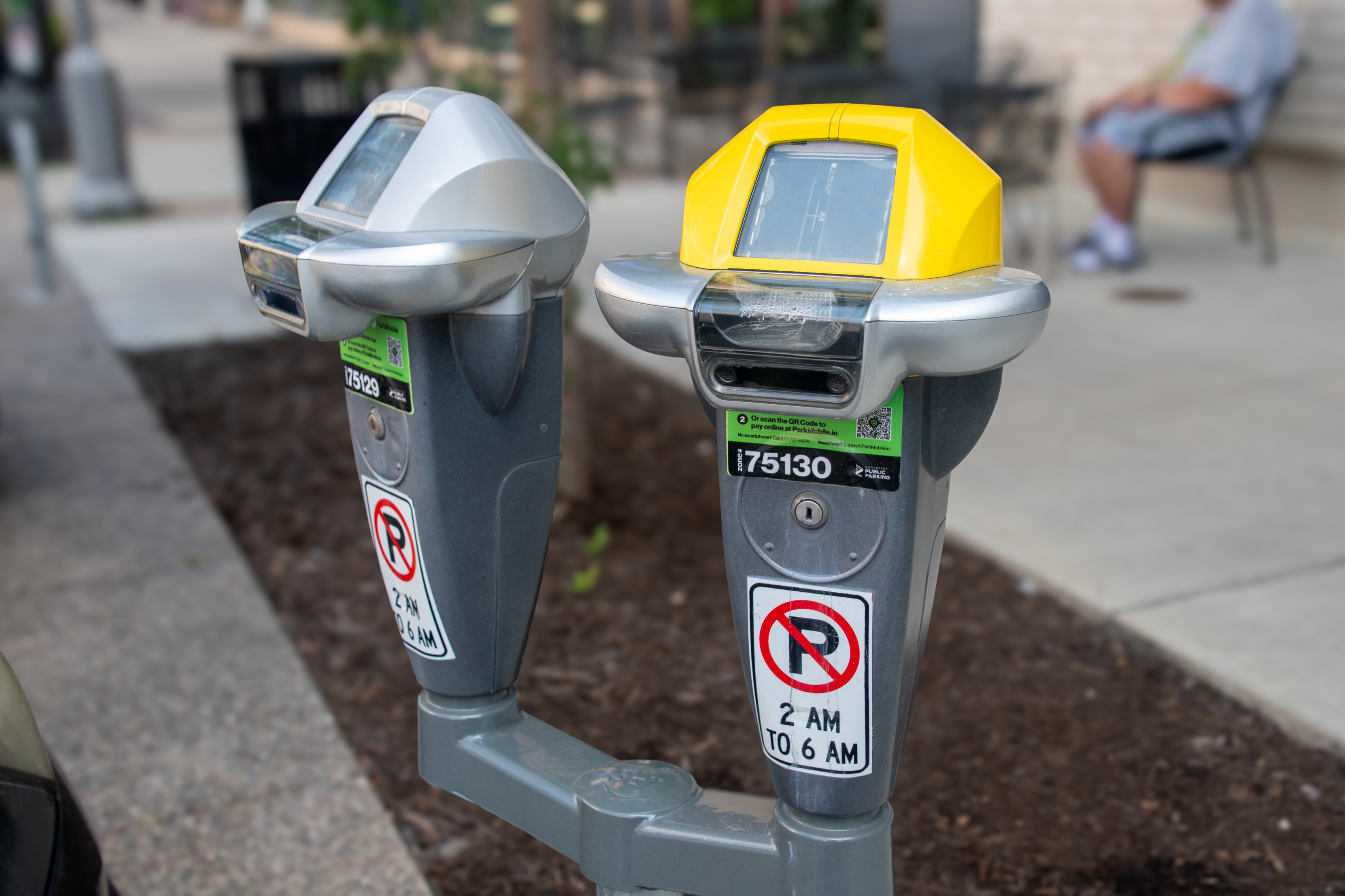 a gray and yellow parking meter near the curb of a downtown sidewalk