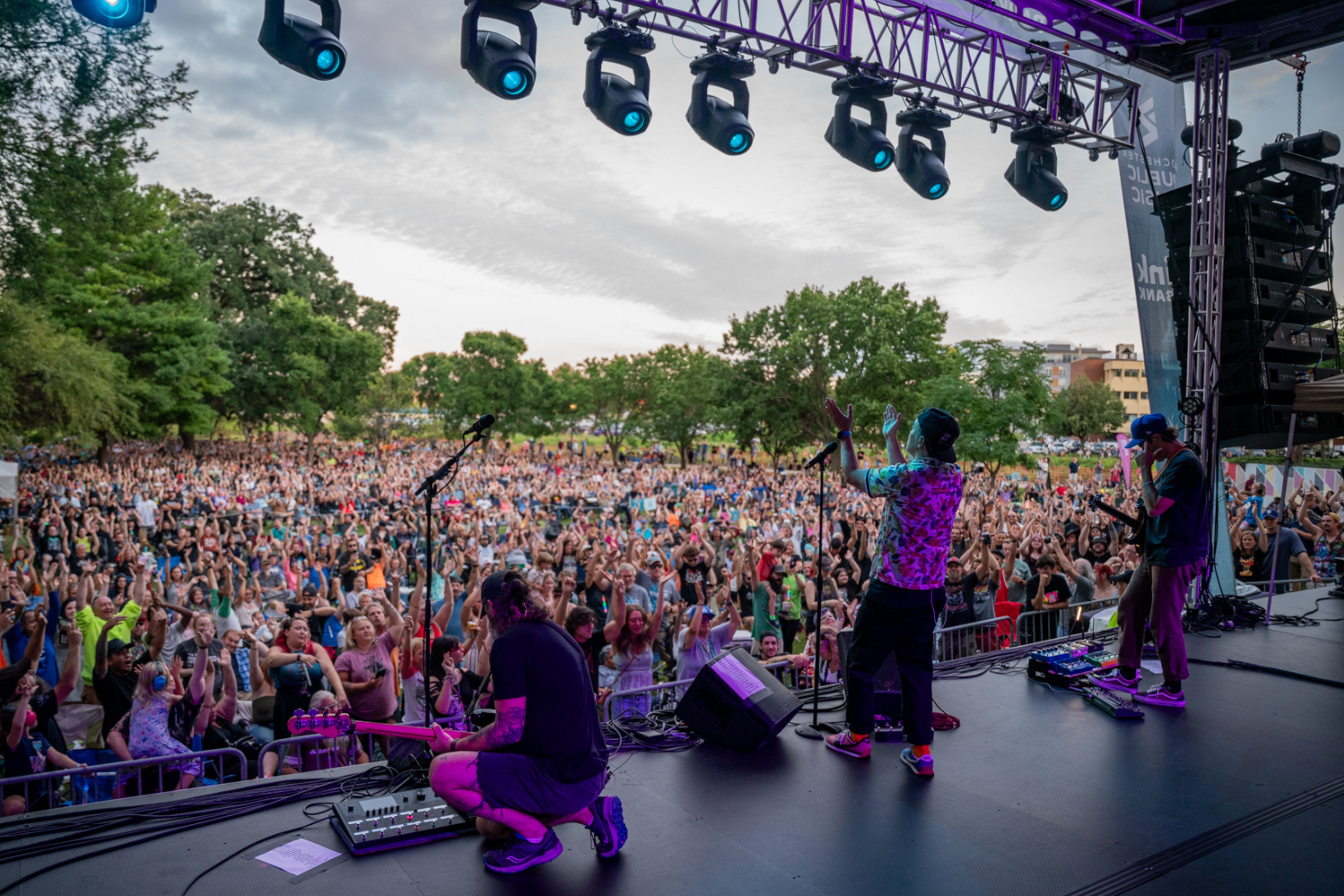 large crowd seen from behind a band of three people, view from stage