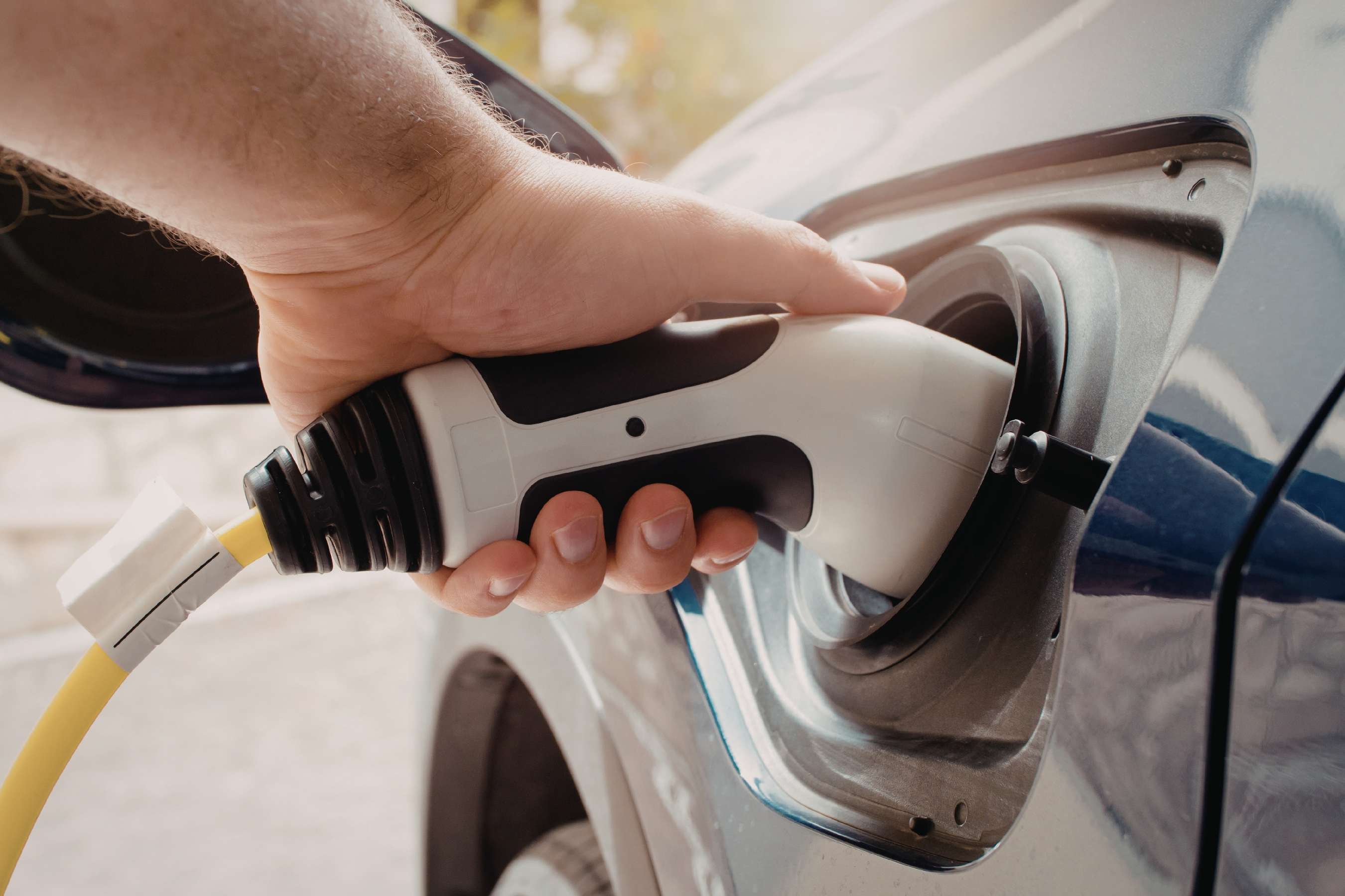 A hand holding a charger to an electric vehicle charging port
