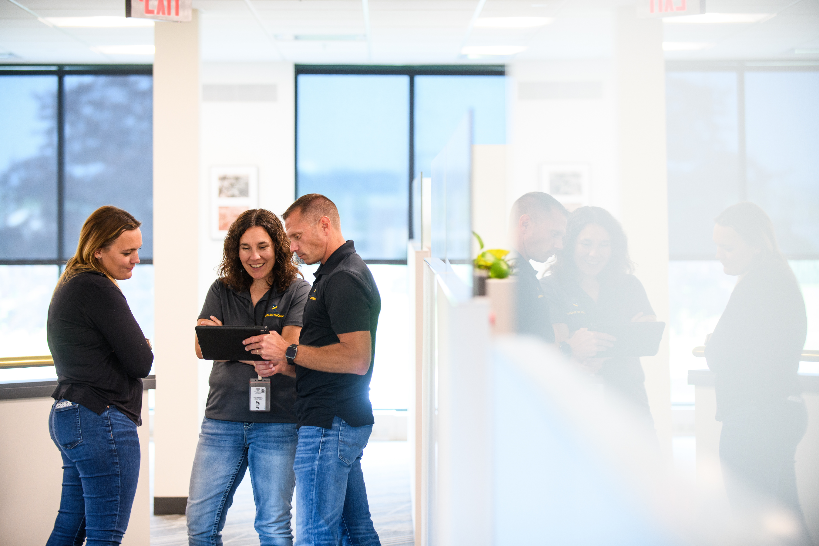 three people looking at a tablet and smiling in a work space