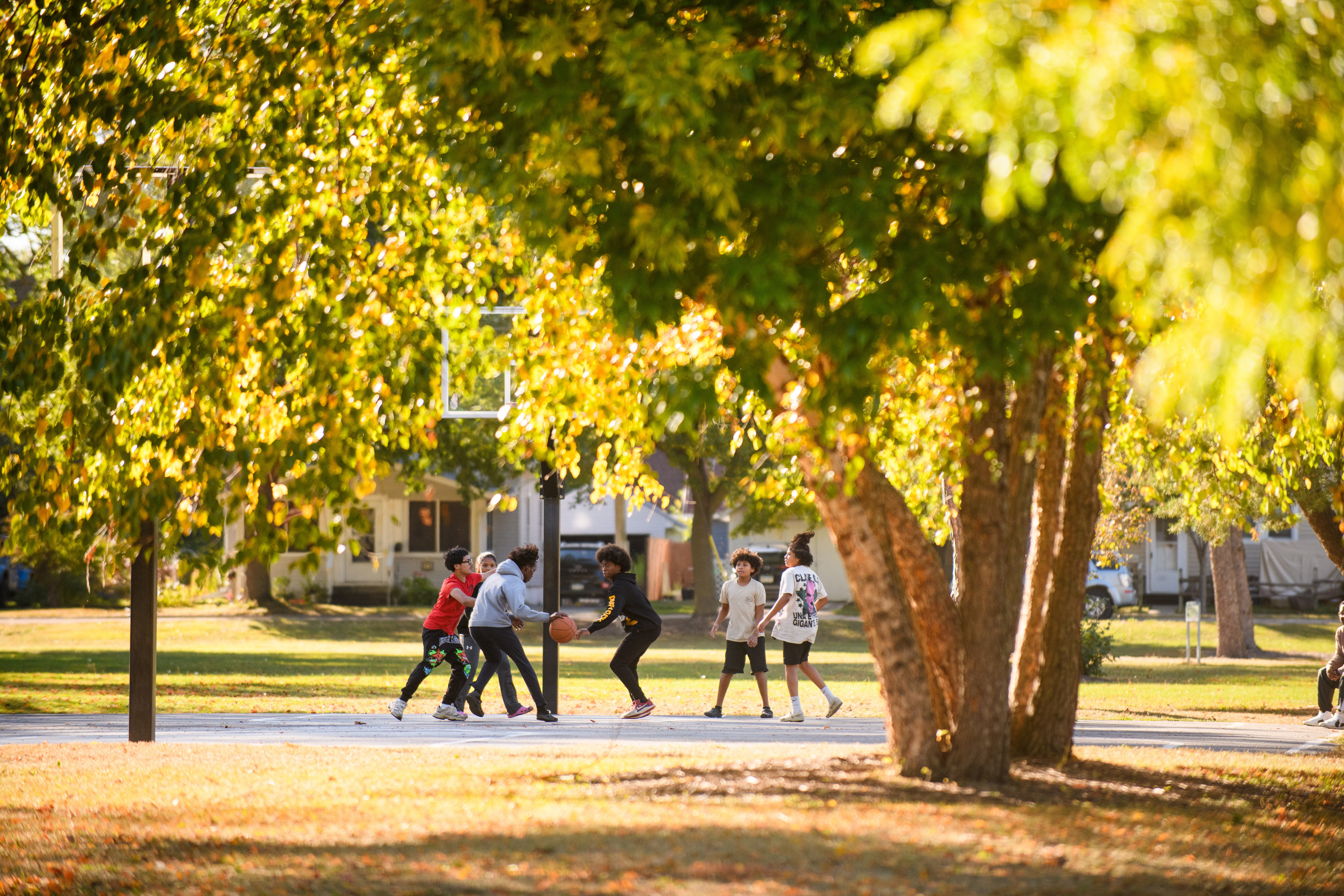 a group of youth playing basketball on an outdoor court on a fall day